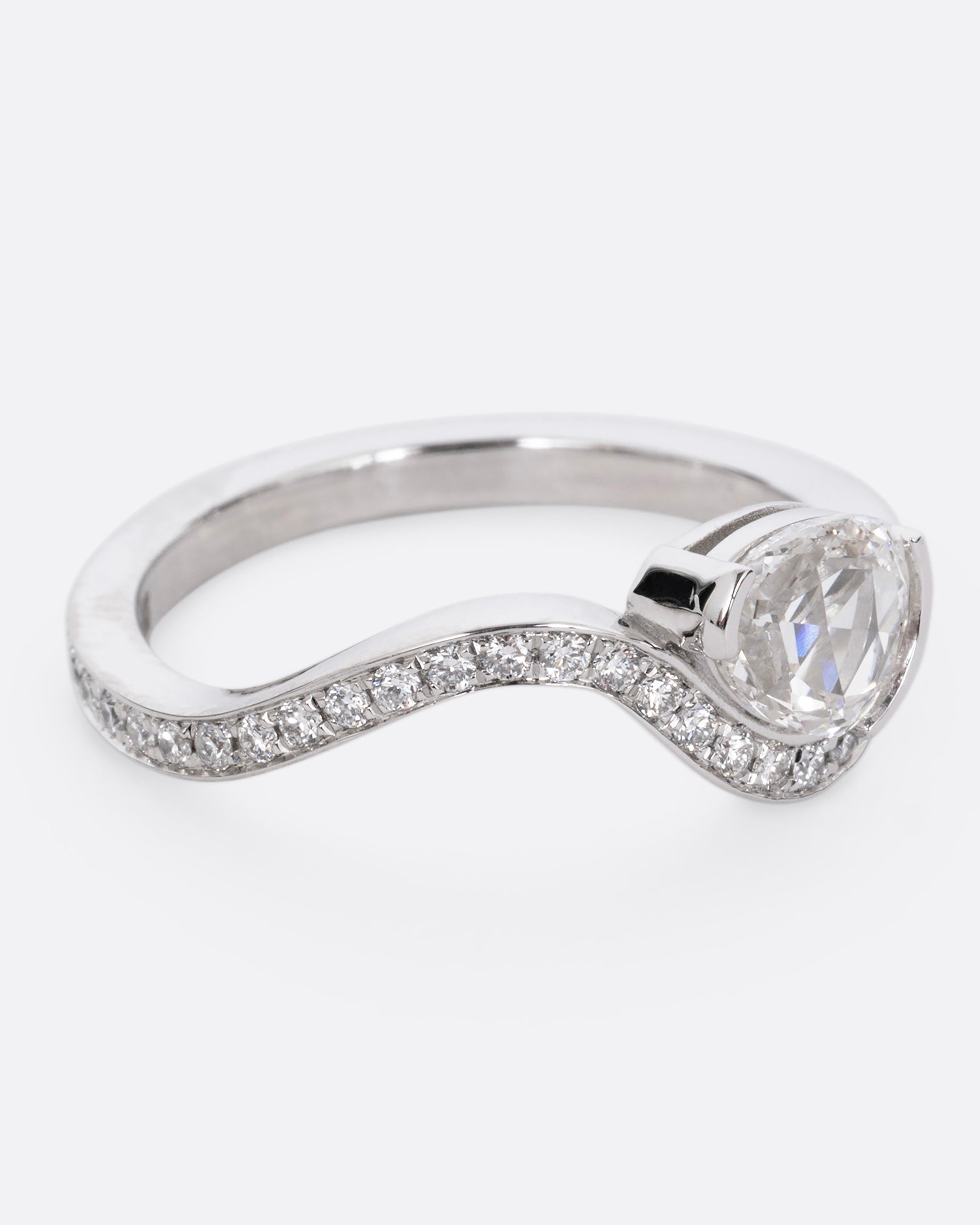 A diamond studded platinum ring with a wavy silhouette and a pear shaped rose cut diamond, shown from the side. 