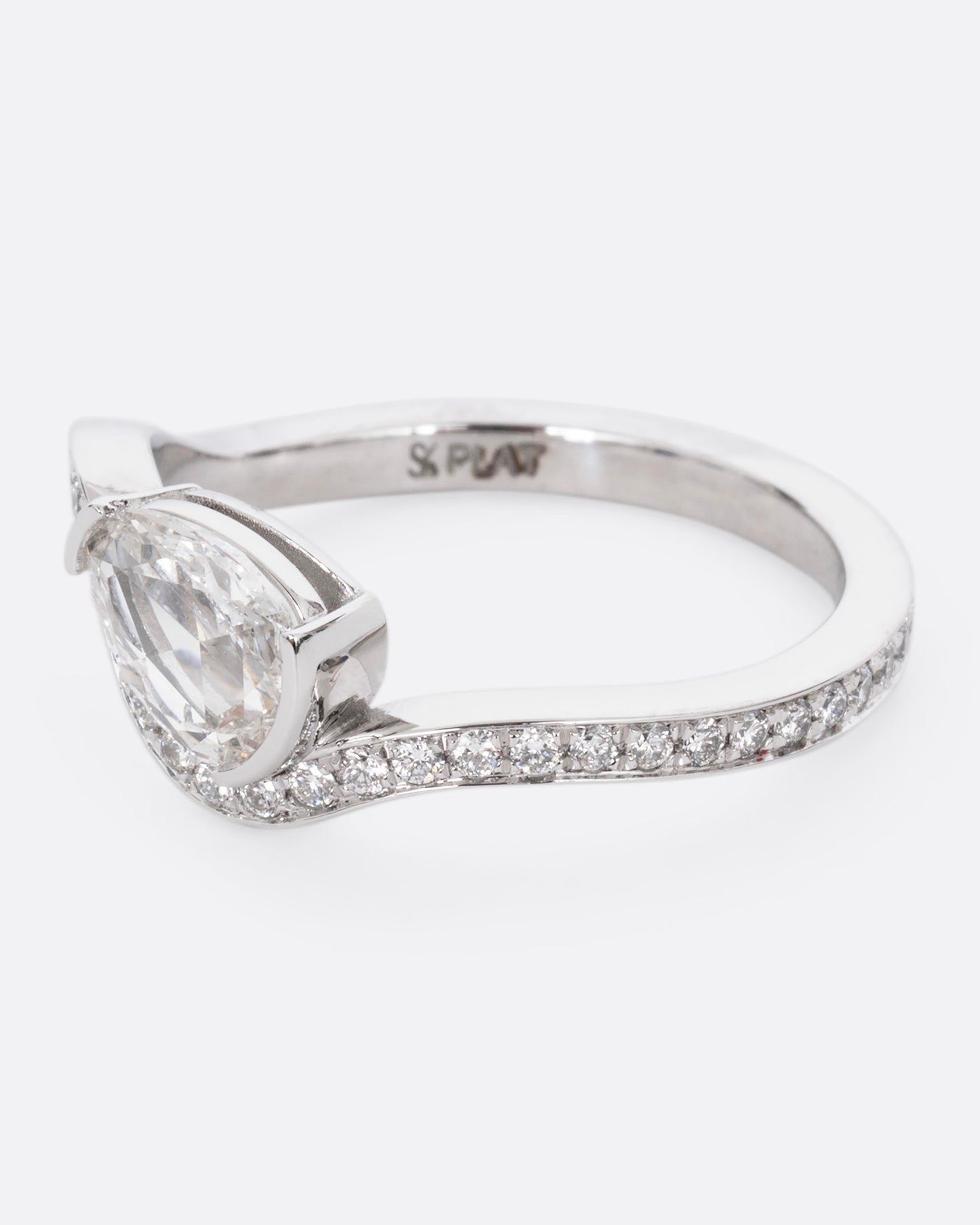 A diamond studded platinum ring with a wavy silhouette and a pear shaped rose cut diamond, shown from the side.