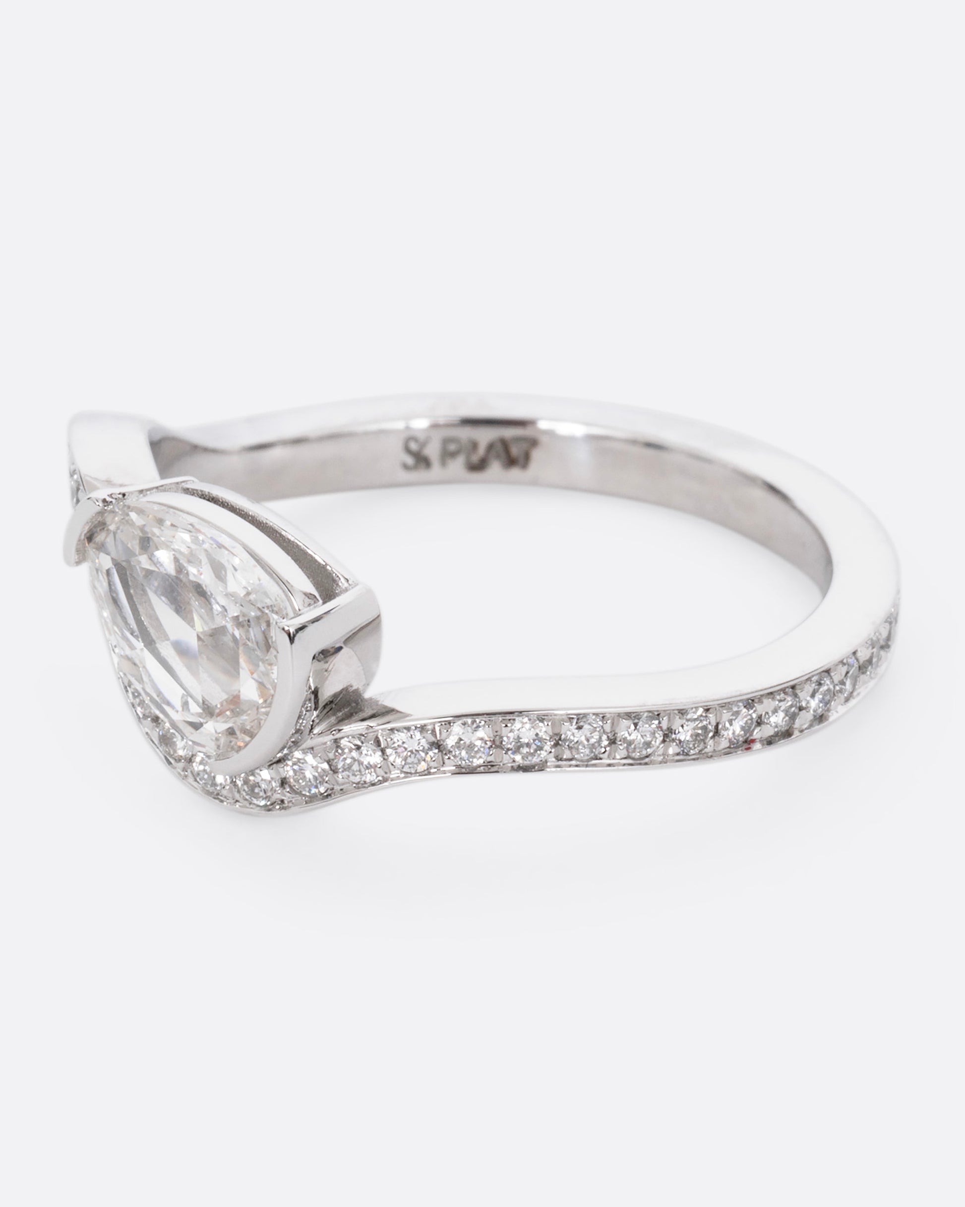 A diamond studded platinum ring with a wavy silhouette and a pear shaped rose cut diamond, shown from the side.