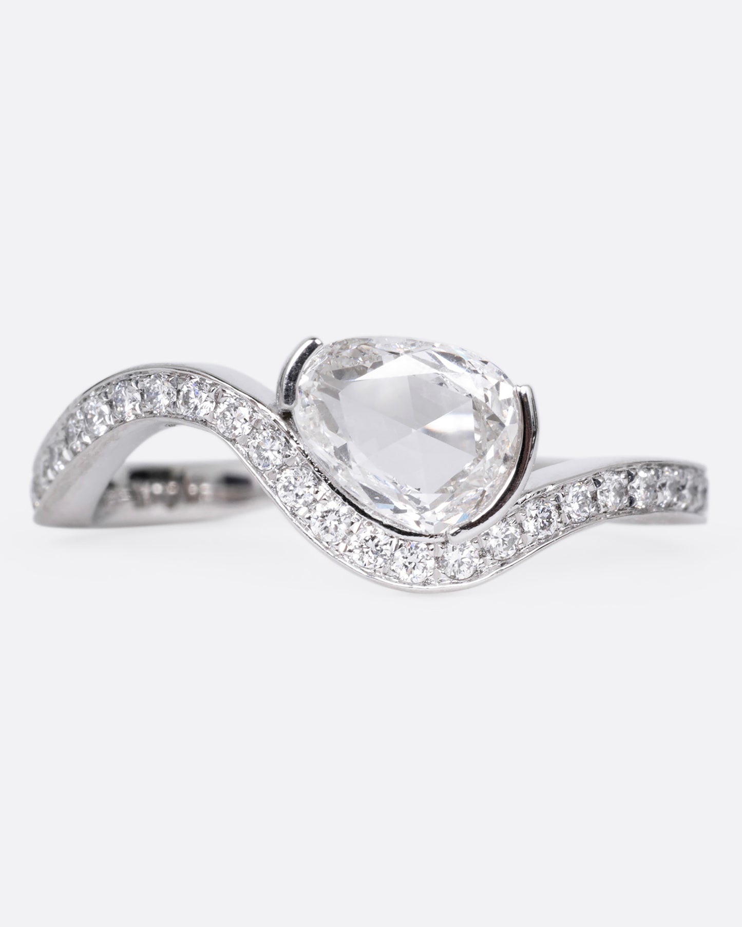 A diamond studded platinum ring with a wavy silhouette and a pear shaped rose cut diamond, shown from the front. 