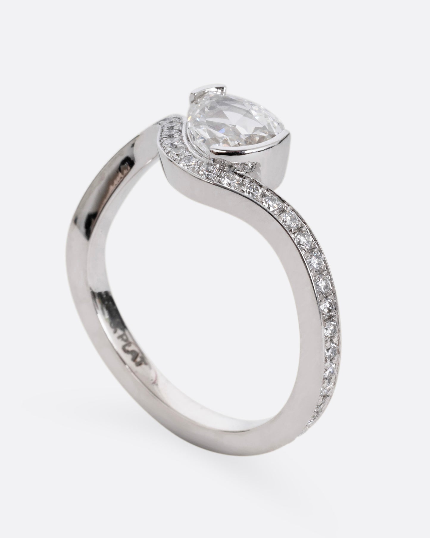 A diamond studded platinum ring with a wavy silhouette and a pear shaped rose cut diamond, shown from the side standing up.