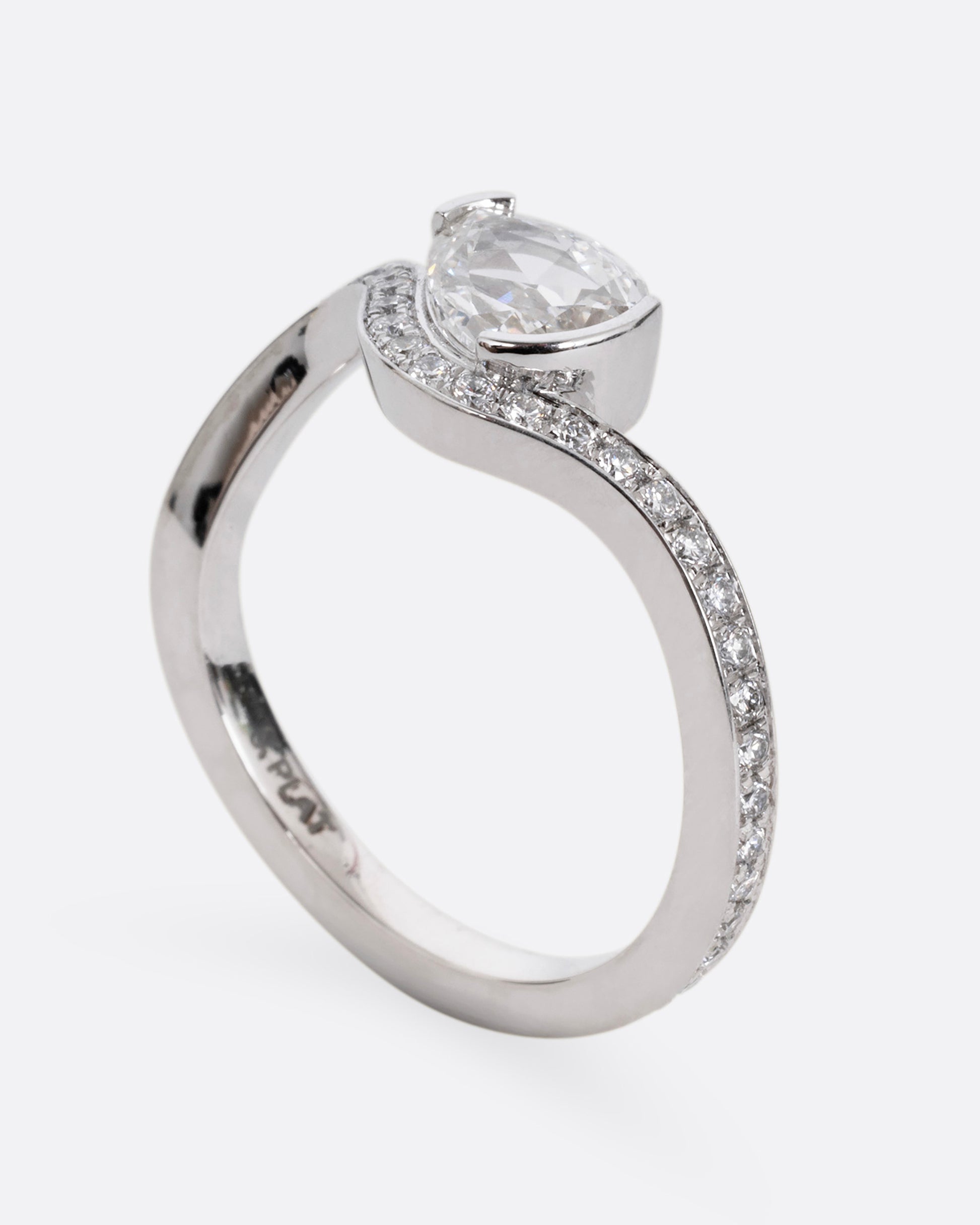 A diamond studded platinum ring with a wavy silhouette and a pear shaped rose cut diamond, shown from the side standing up.
