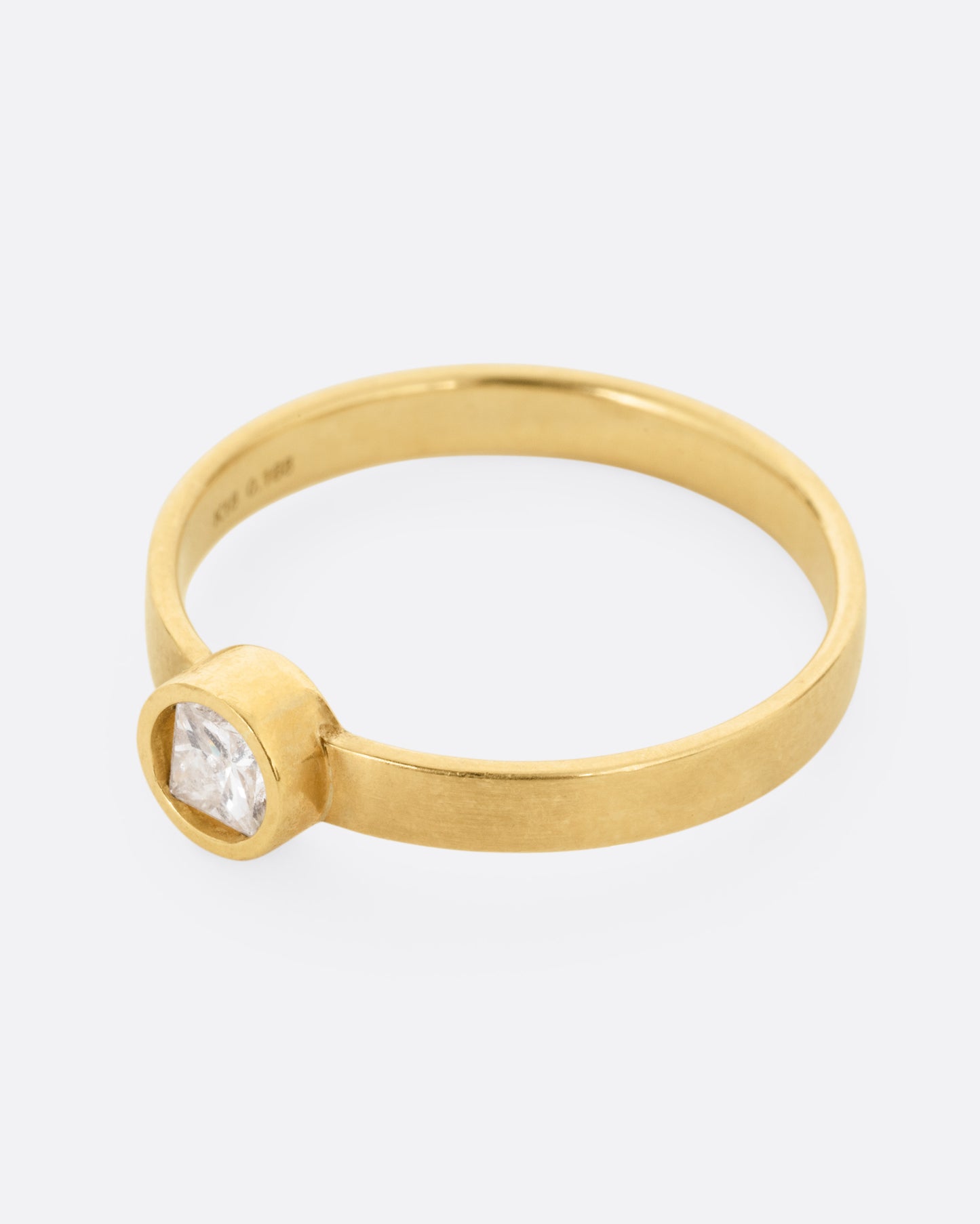 side view of a round yellow gold hole has a diamond set floating into the middle of it. there is a medium wide band that the setting is attached to and the gold is matte.