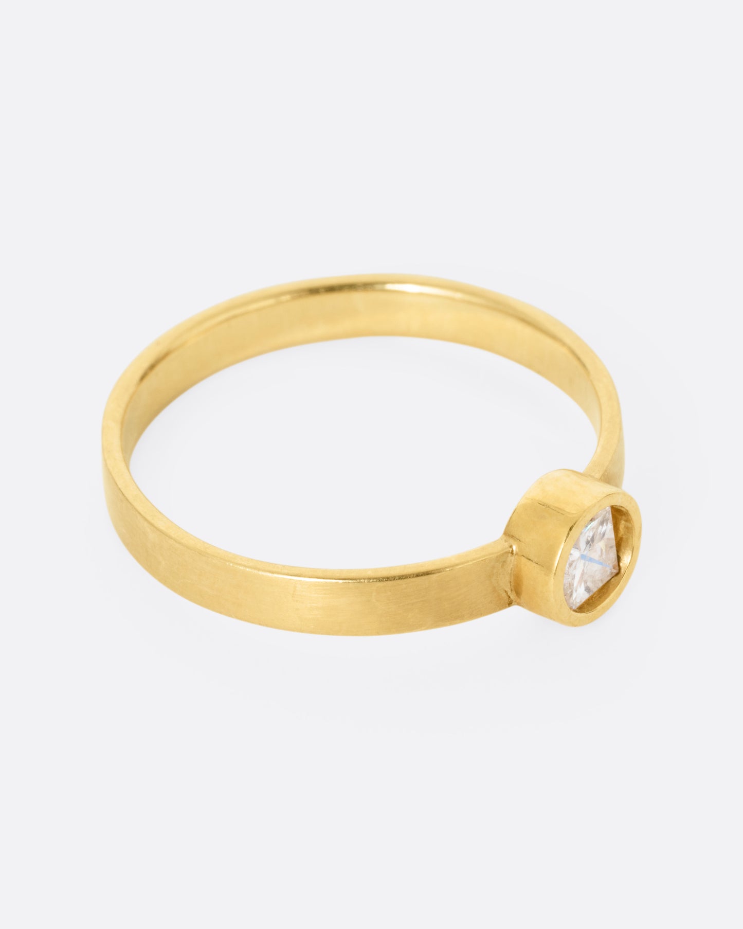 side view of a round yellow gold hole has a diamond set floating into the middle of it. there is a medium wide band that the setting is attached to and the gold is matte.