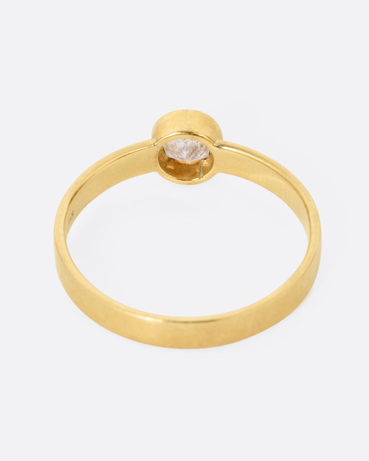 back view of a round yellow gold hole has a diamond set floating into the middle of it. there is a medium wide band that the setting is attached to and the gold is matte.