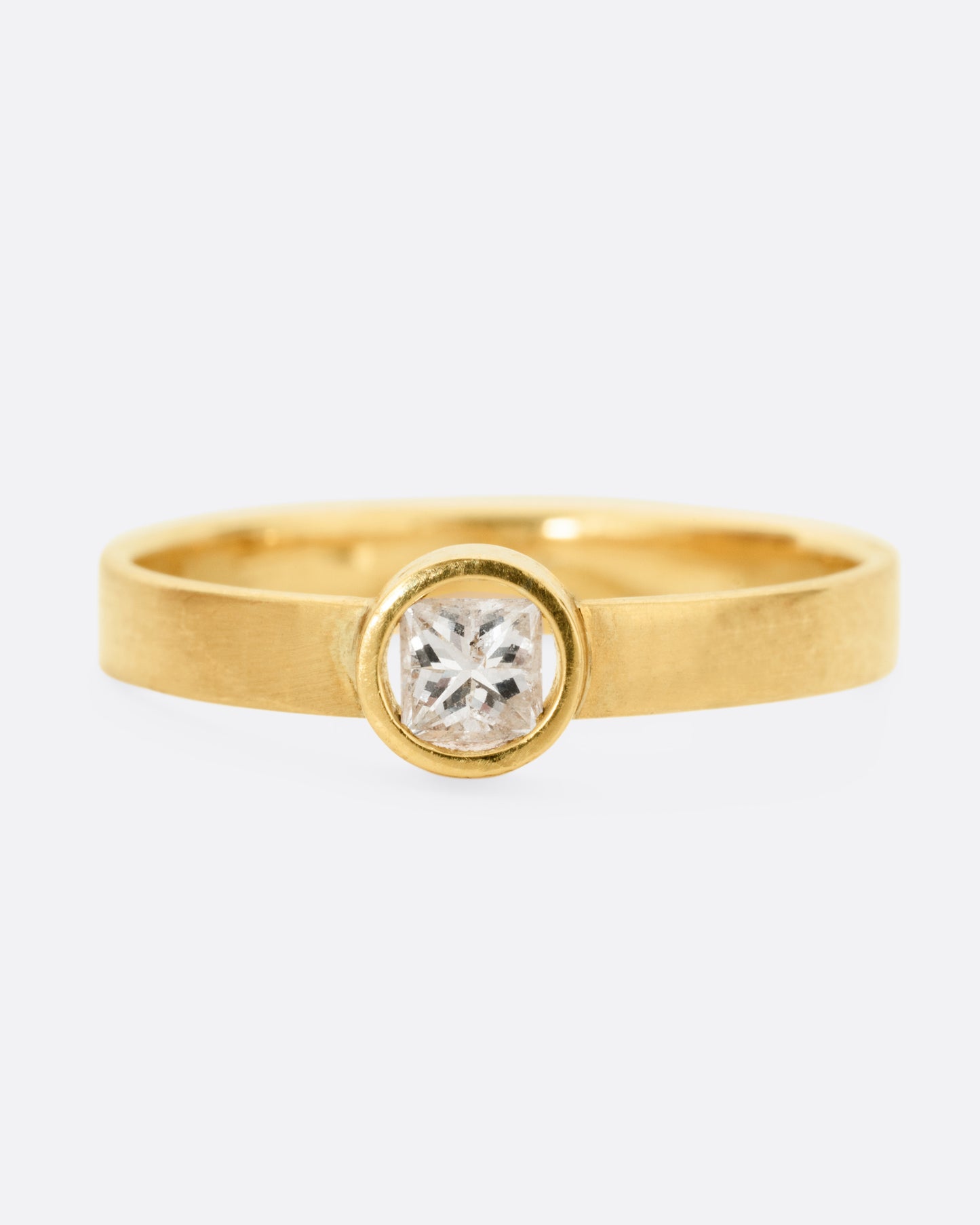 front view of a round yellow gold hole has a diamond set floating into the middle of it. there is a medium wide band that the setting is attached to and the gold is matte.