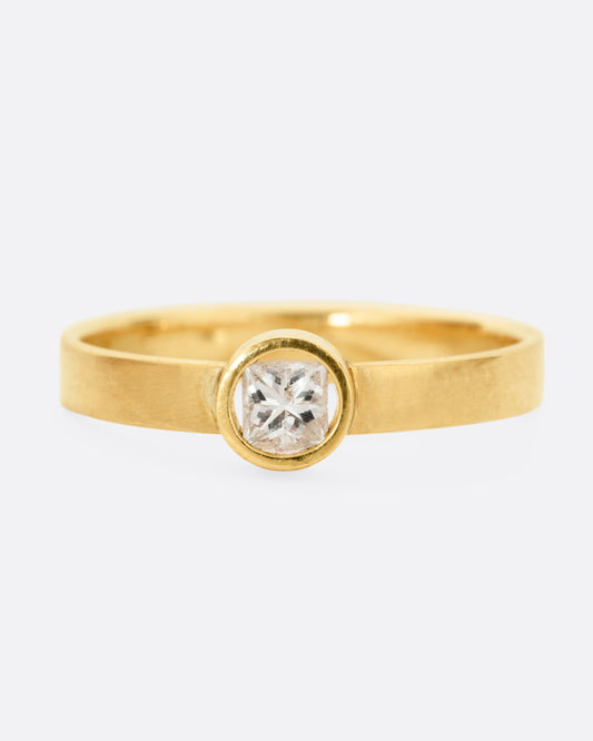 front view of a round yellow gold hole has a diamond set floating into the middle of it. there is a medium wide band that the setting is attached to and the gold is matte.
