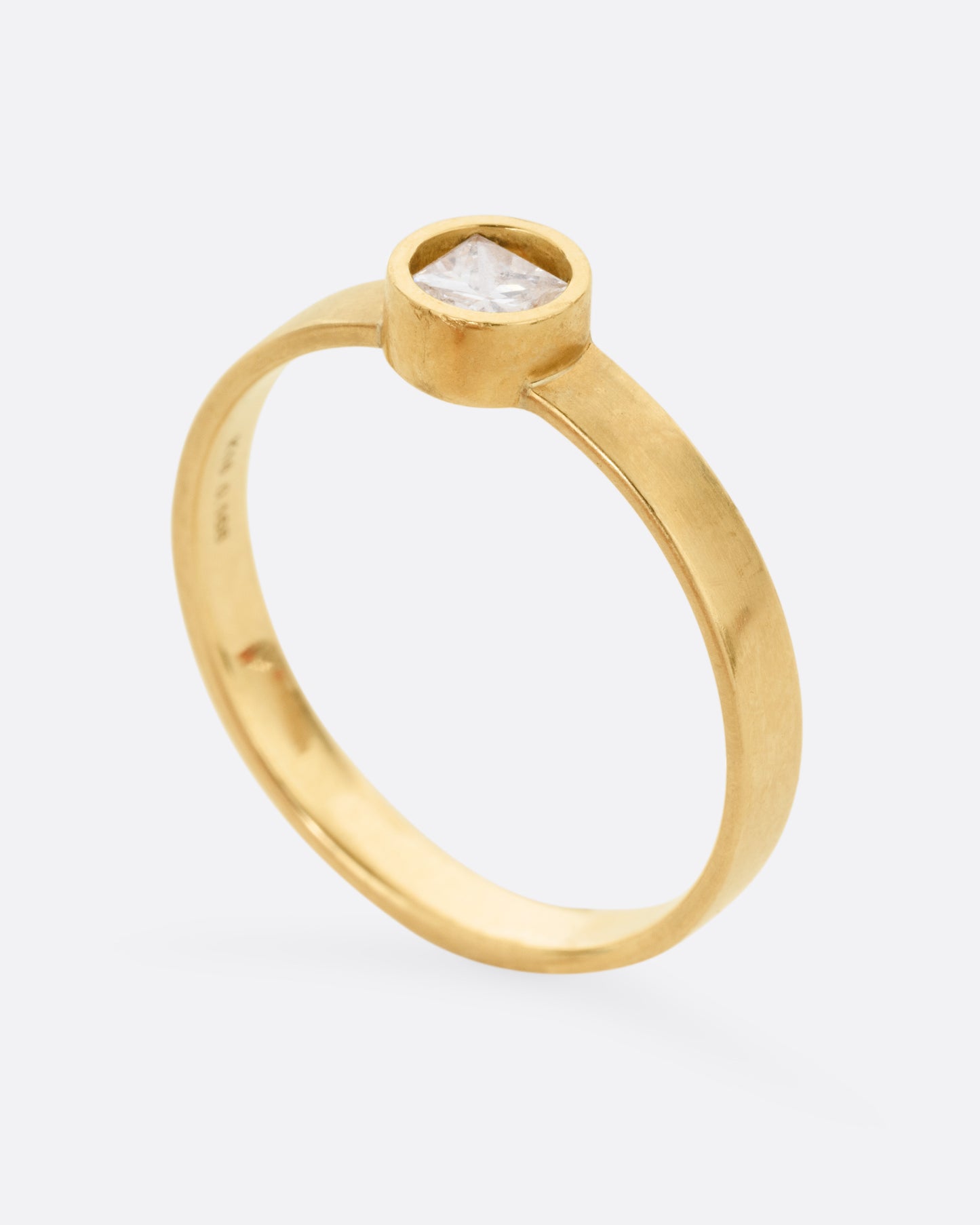 standing view of a round yellow gold hole has a diamond set floating into the middle of it. there is a medium wide band that the setting is attached to and the gold is matte.