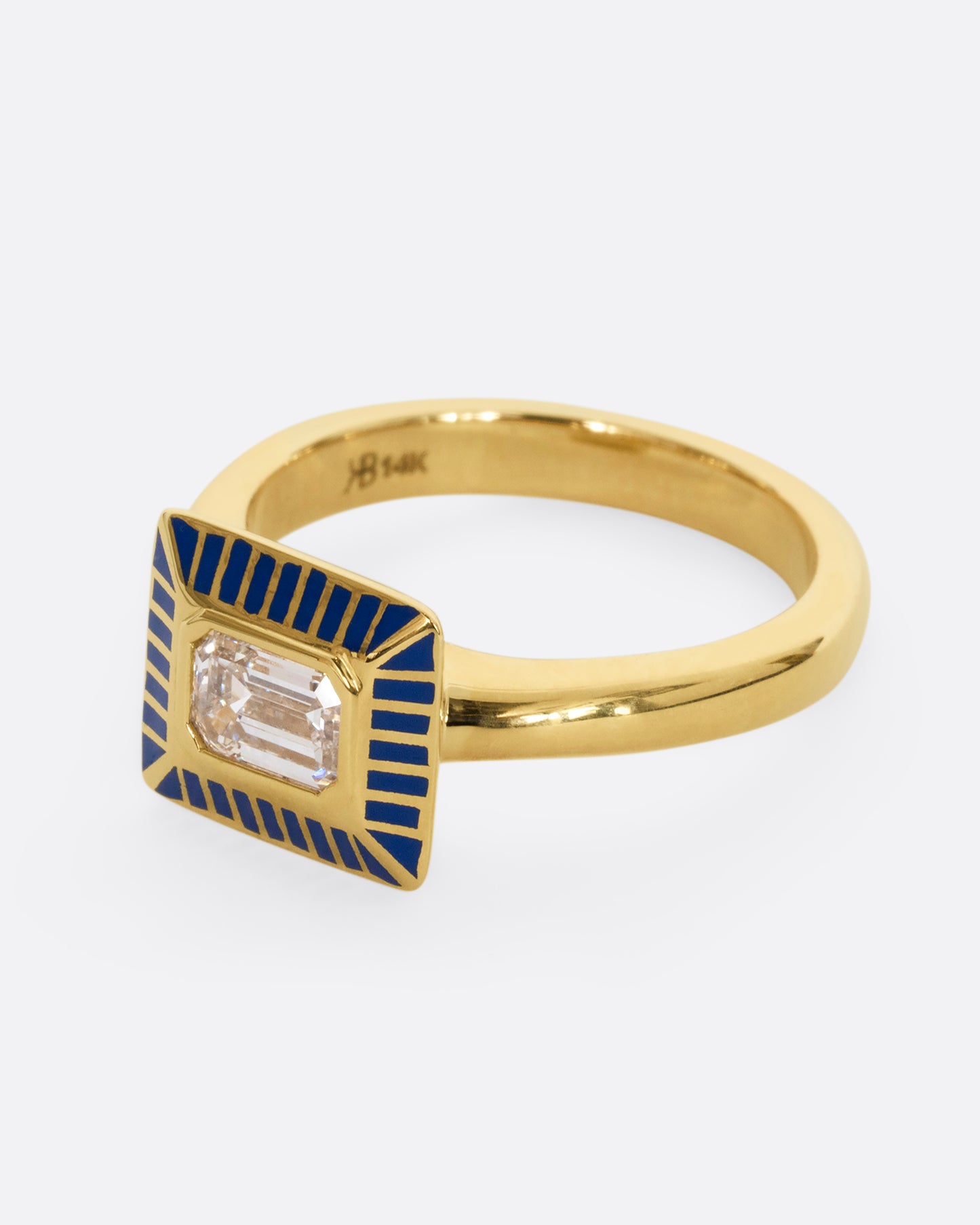 A yellow gold ring with an emerald cut diamond in a blue enamel striped rectangular setting. Shown from the side.