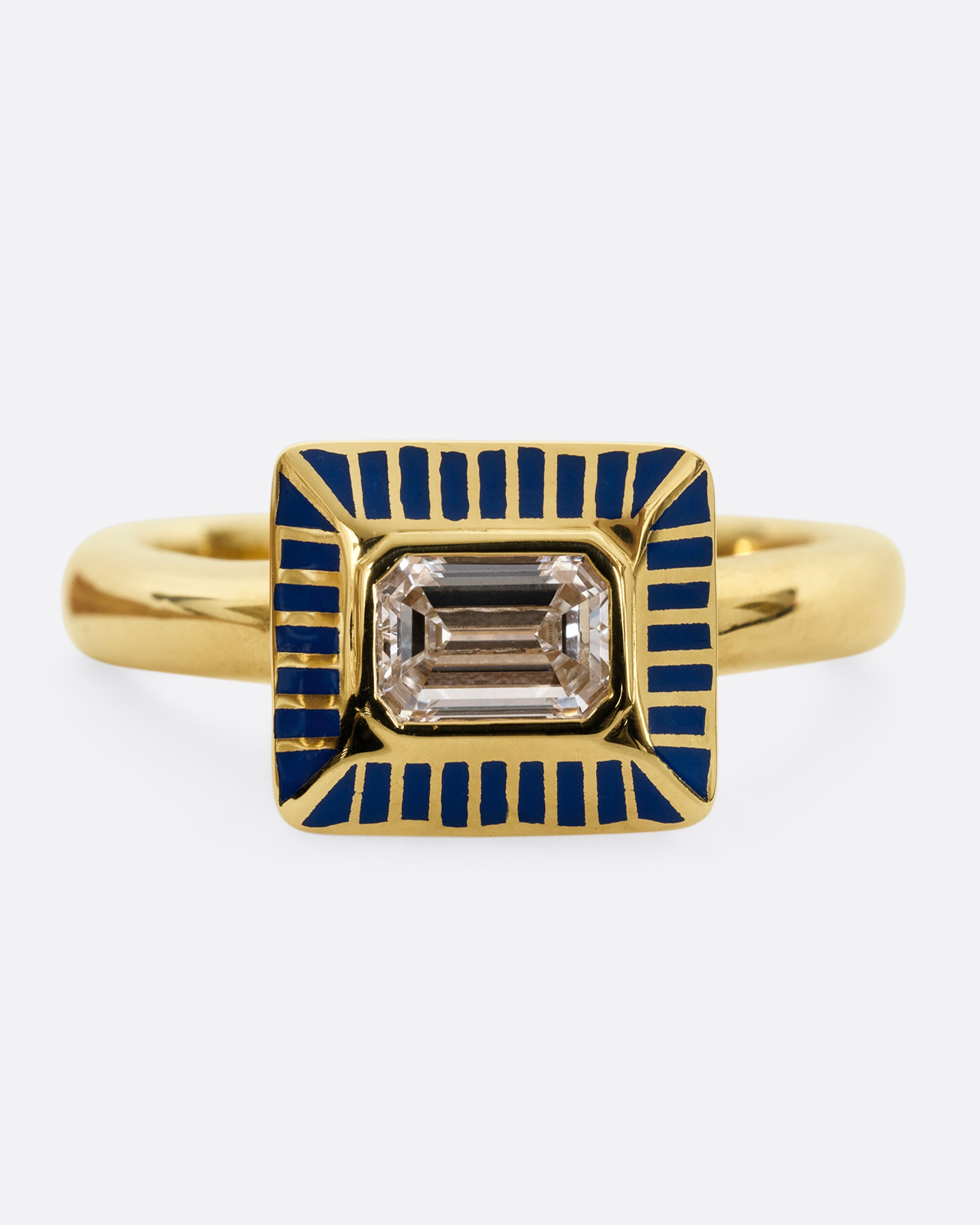 A yellow gold ring with an emerald cut diamond in a blue enamel striped rectangular setting. Shown from the front.