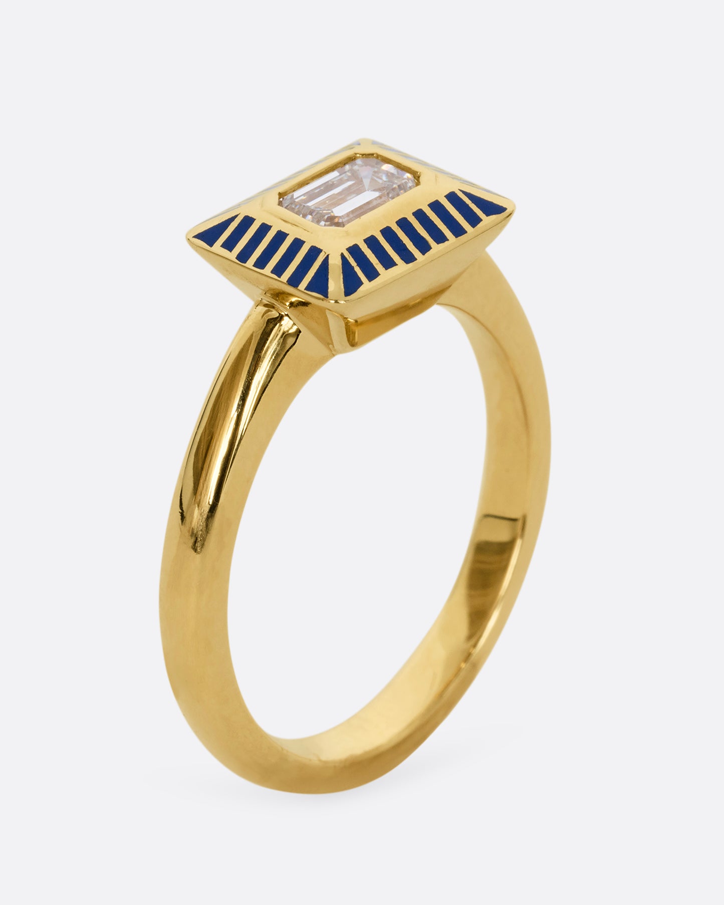 A yellow gold ring with an emerald cut diamond in a blue enamel striped rectangular setting. Shown from the side.