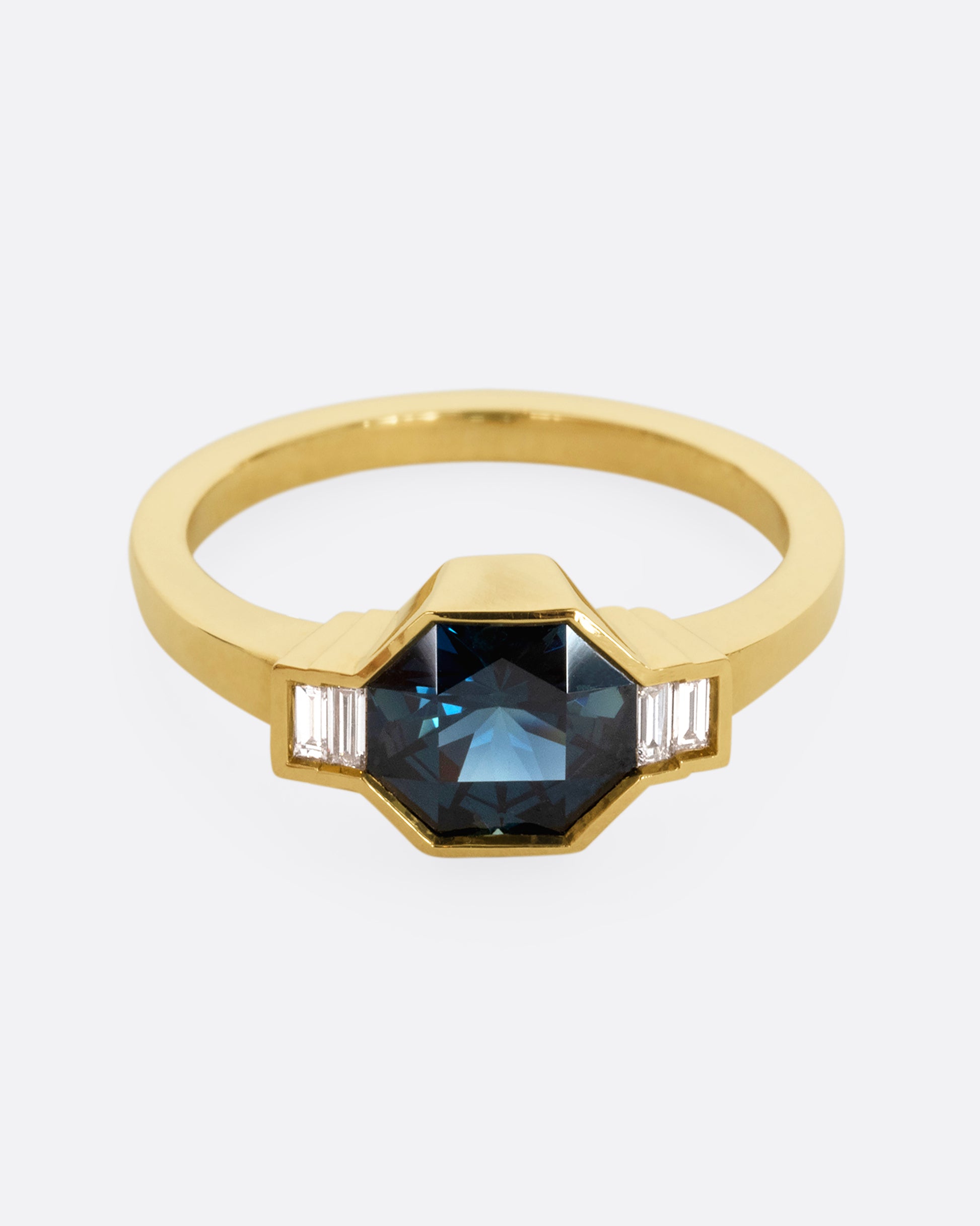 A yellow gold ring with a sapphire at the center and baguette diamonds on either side. Shown from the front.