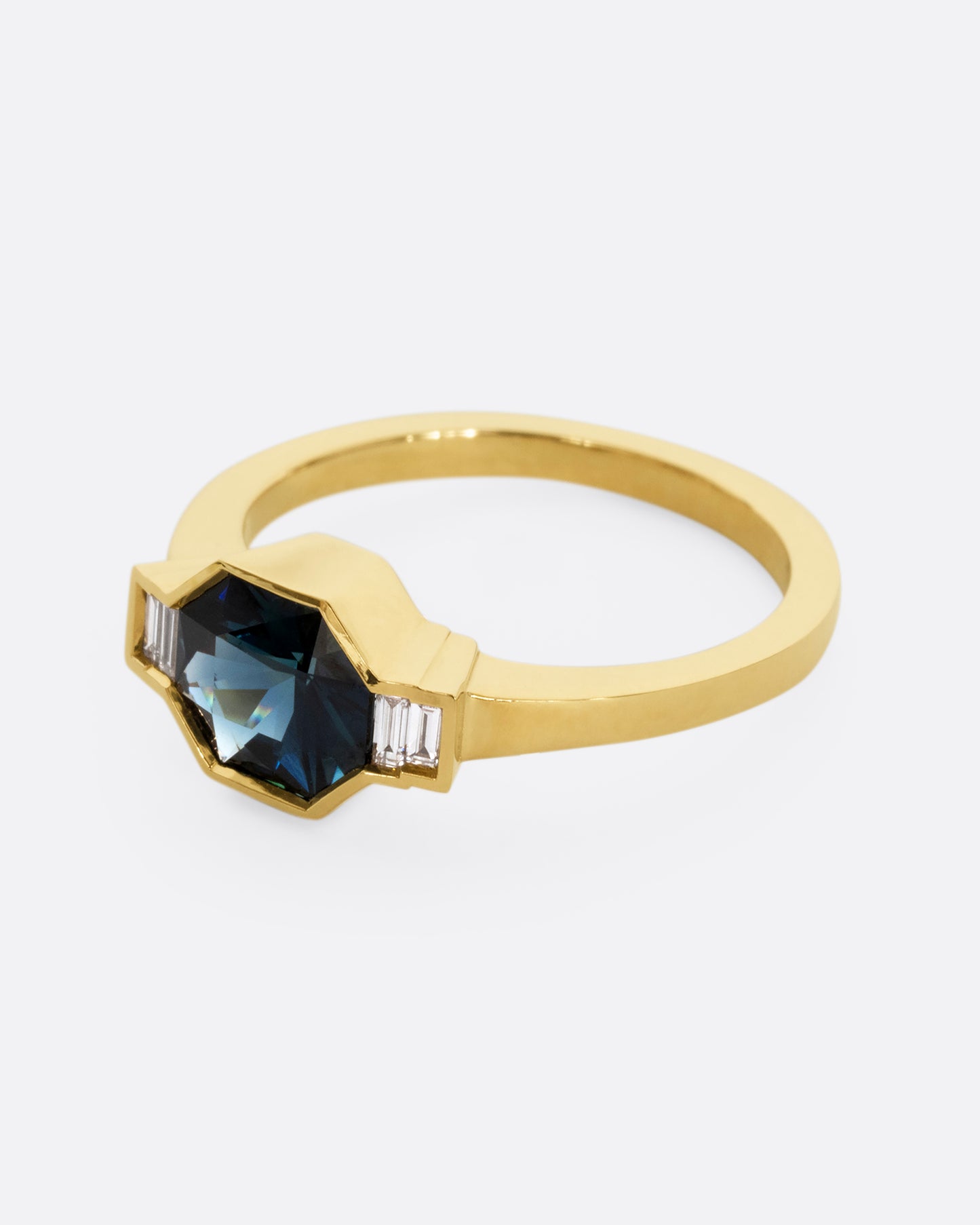 A yellow gold ring with a sapphire at the center and baguette diamonds on either side. Shown from the side.