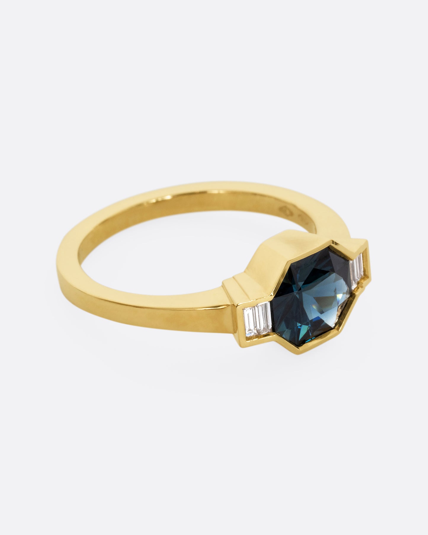 A yellow gold ring with a sapphire at the center and baguette diamonds on either side. Shown from the side.