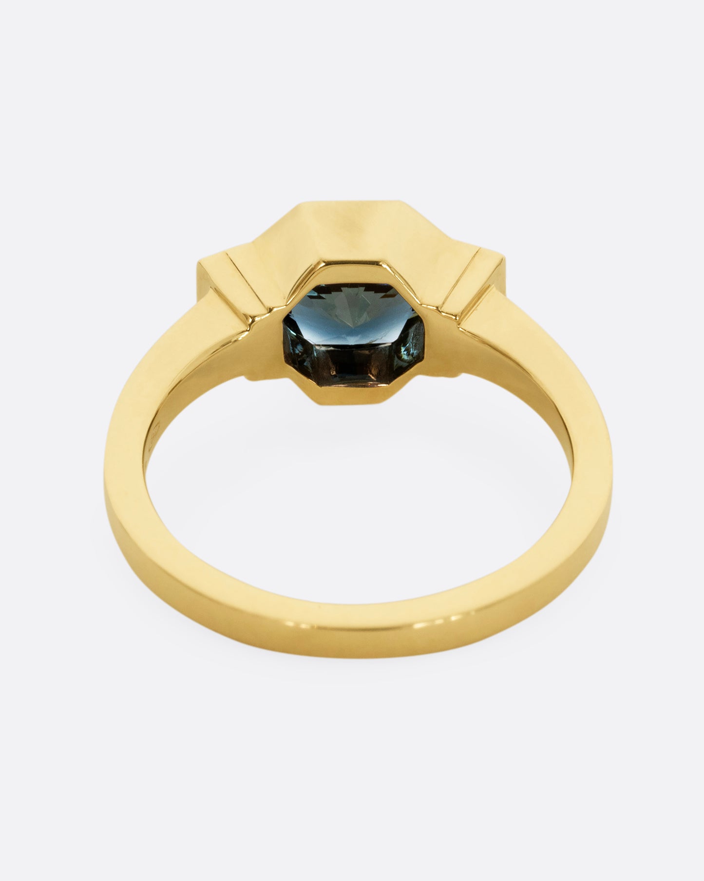 A yellow gold ring with a sapphire at the center and baguette diamonds on either side. Shown from the back.