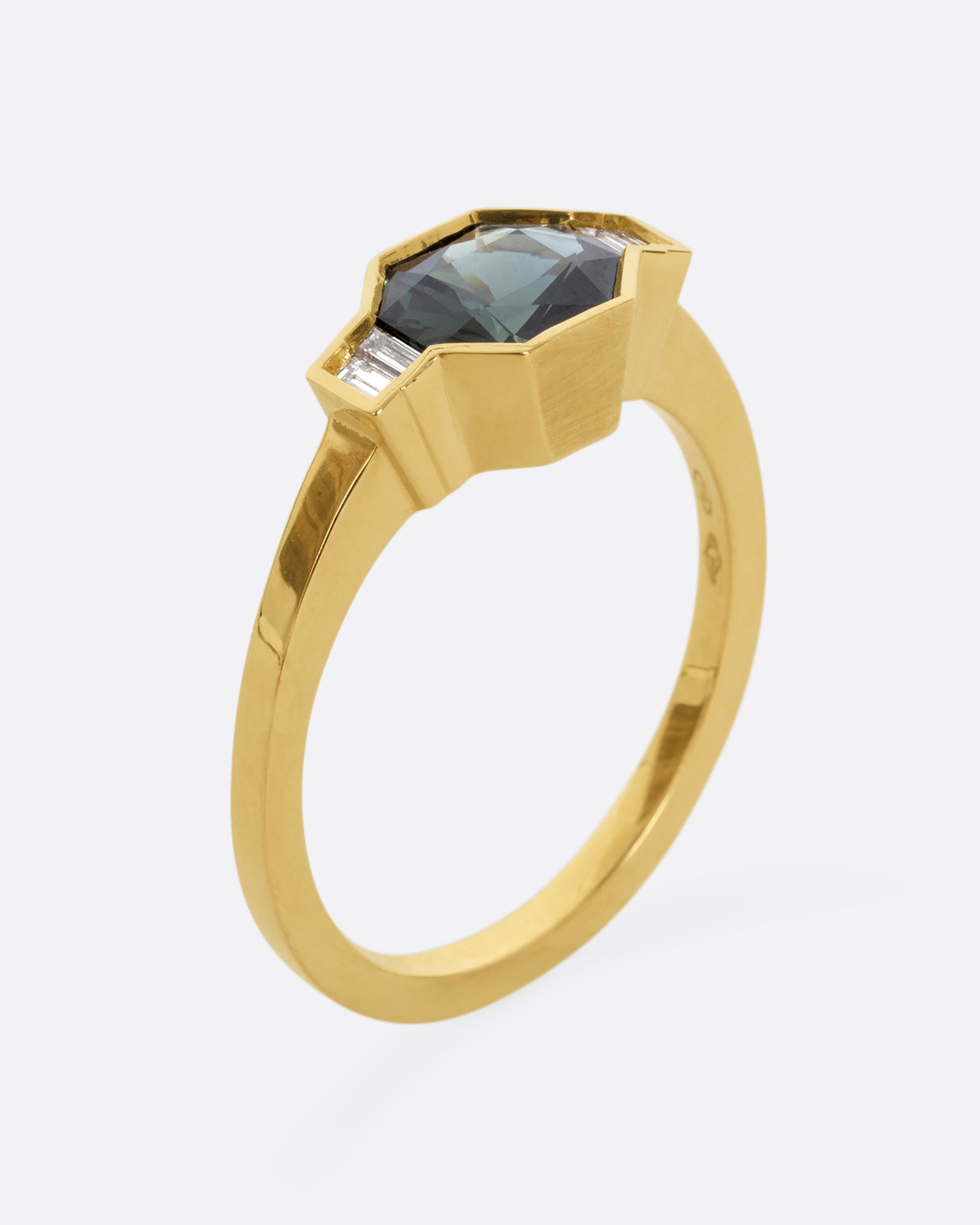 A yellow gold ring with a sapphire at the center and baguette diamonds on either side. Shown from the side, standing up.