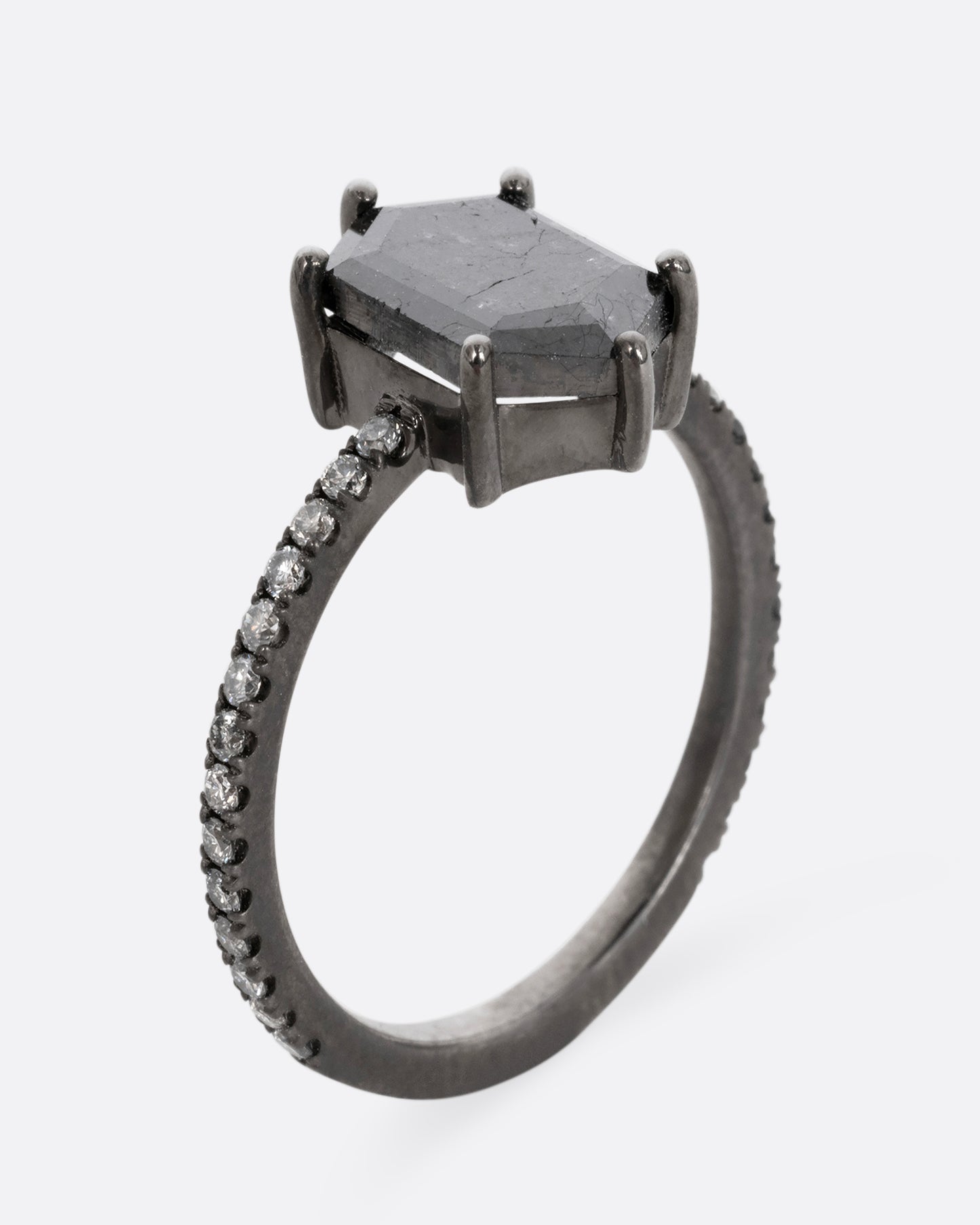 A rhodium finished white gold ring with a single black diamond and a pave diamond band. Shown from the side, standing up.