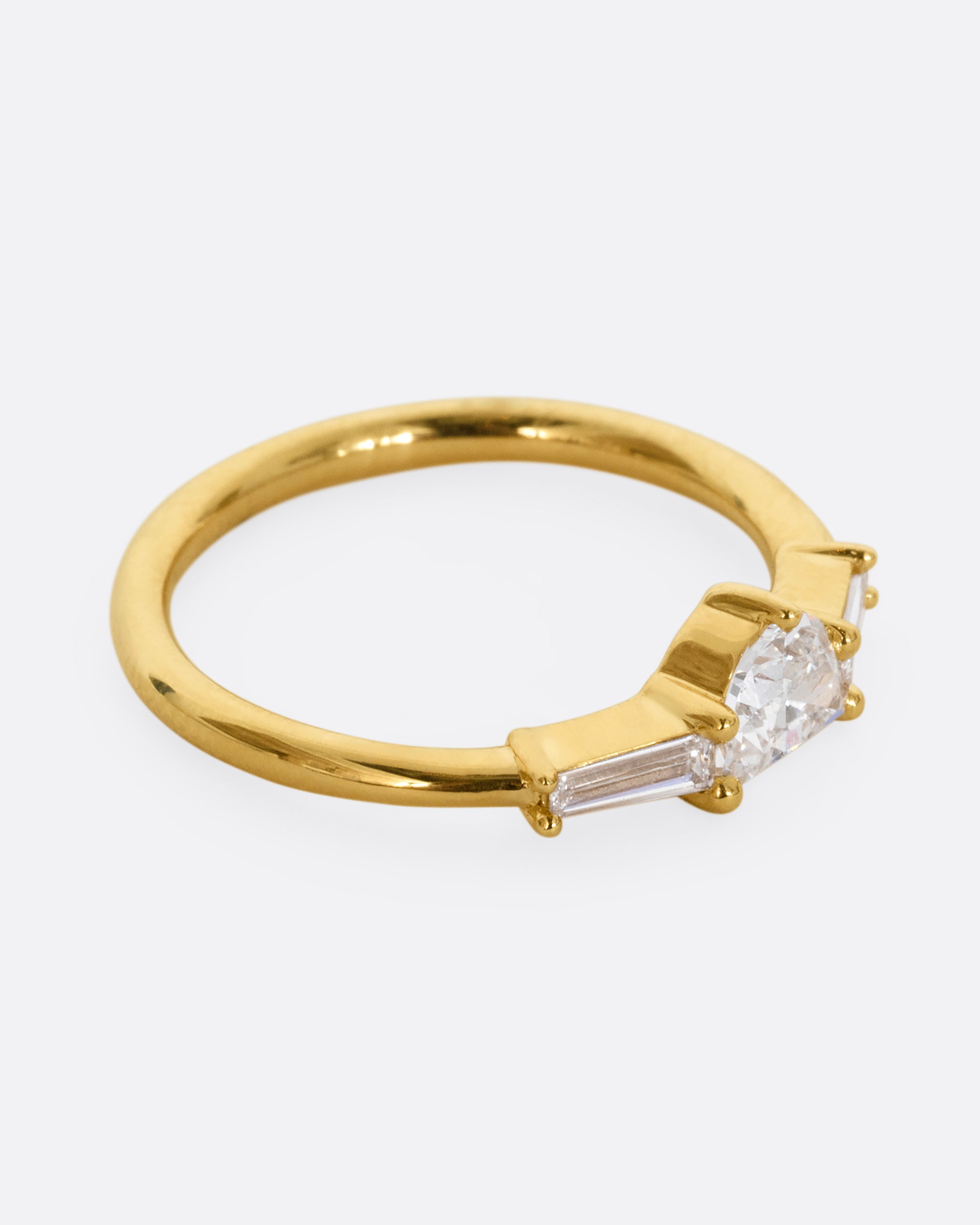 A yellow gold ring with a half moon shaped diamond and two baguette diamonds. Shown from the side.