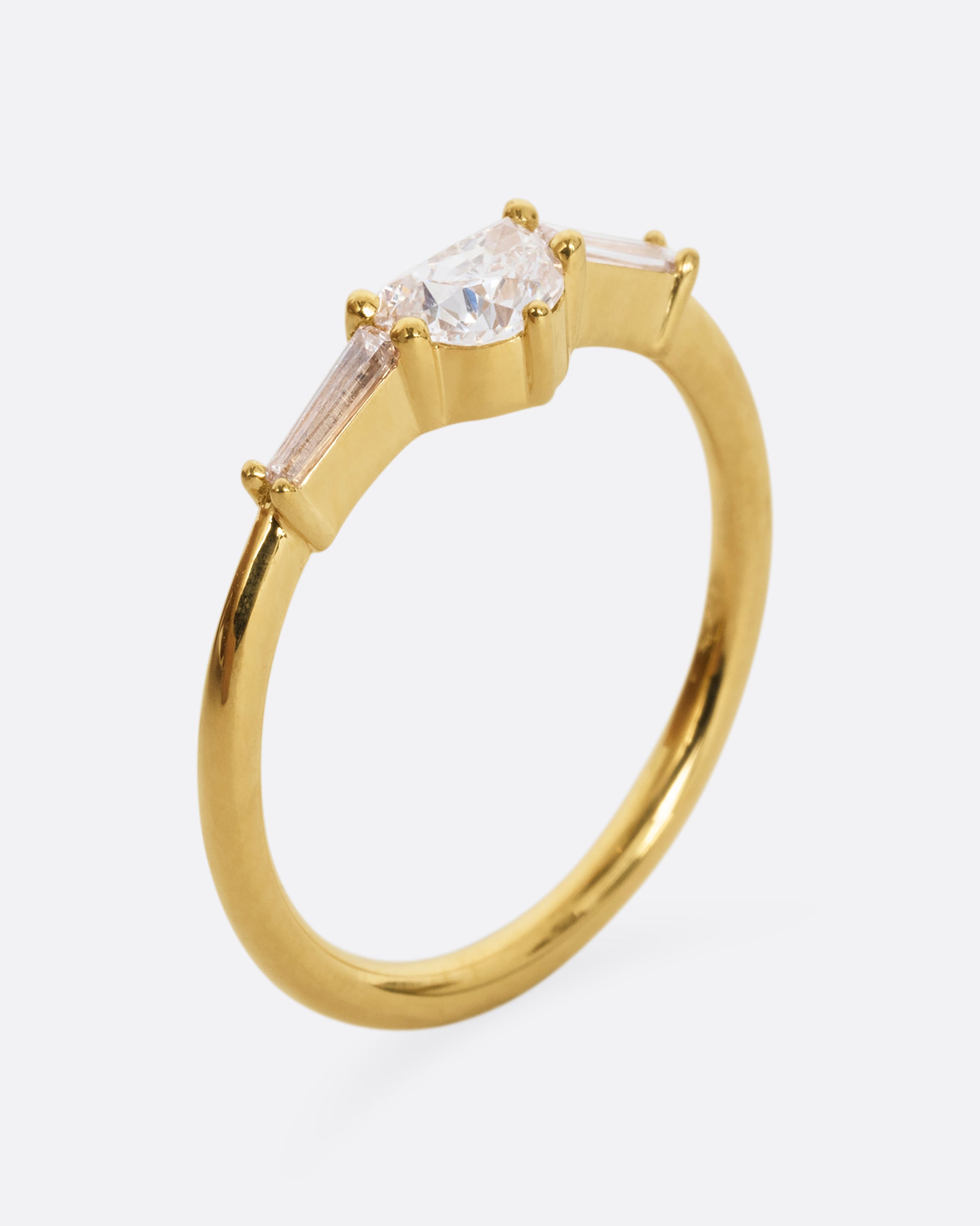 A yellow gold ring with a half moon shaped diamond and two baguette diamonds. Shown from the side, standing up.