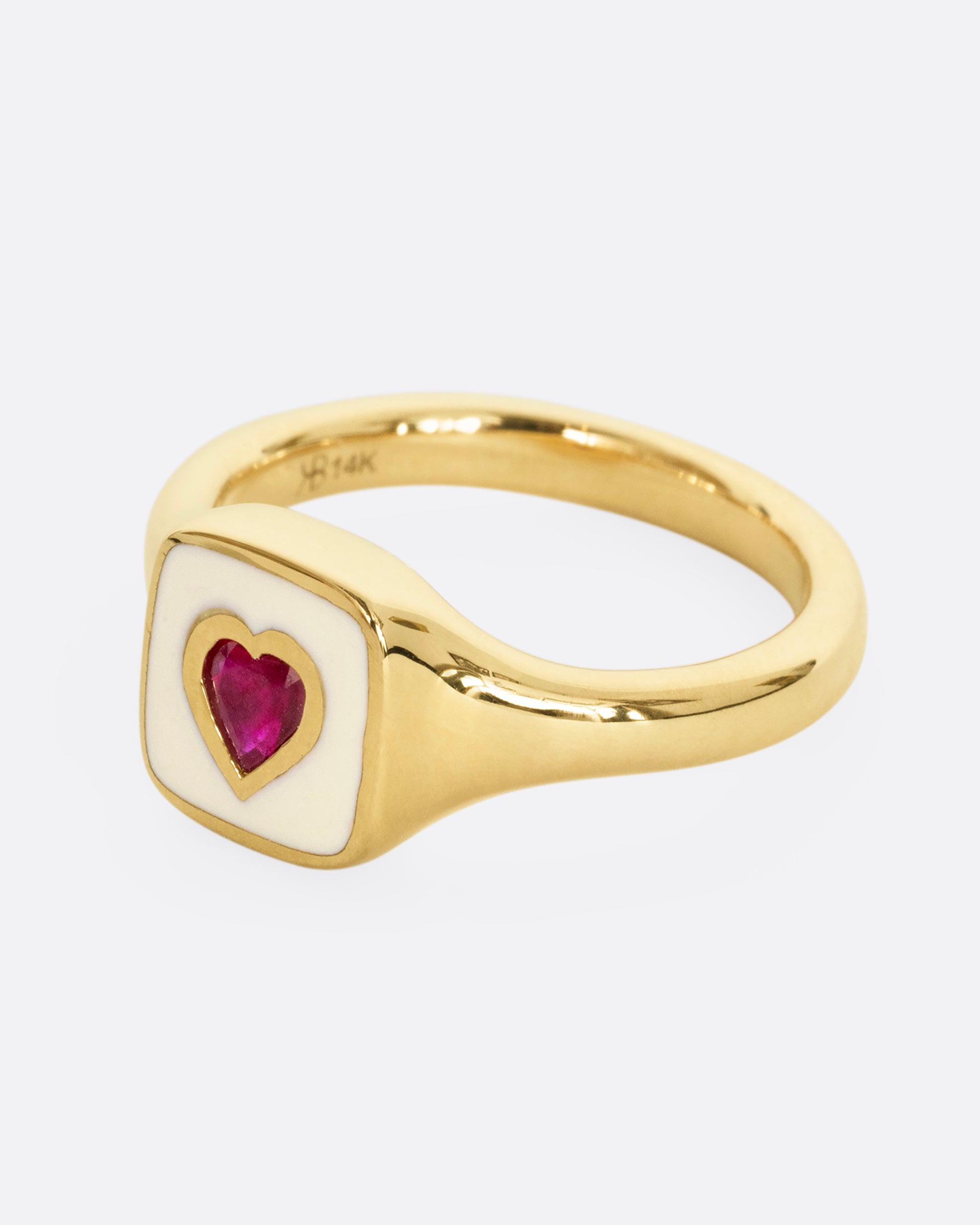 A yellow gold signet ring with cream enamel and a heart shaped ruby. Shown from the side.