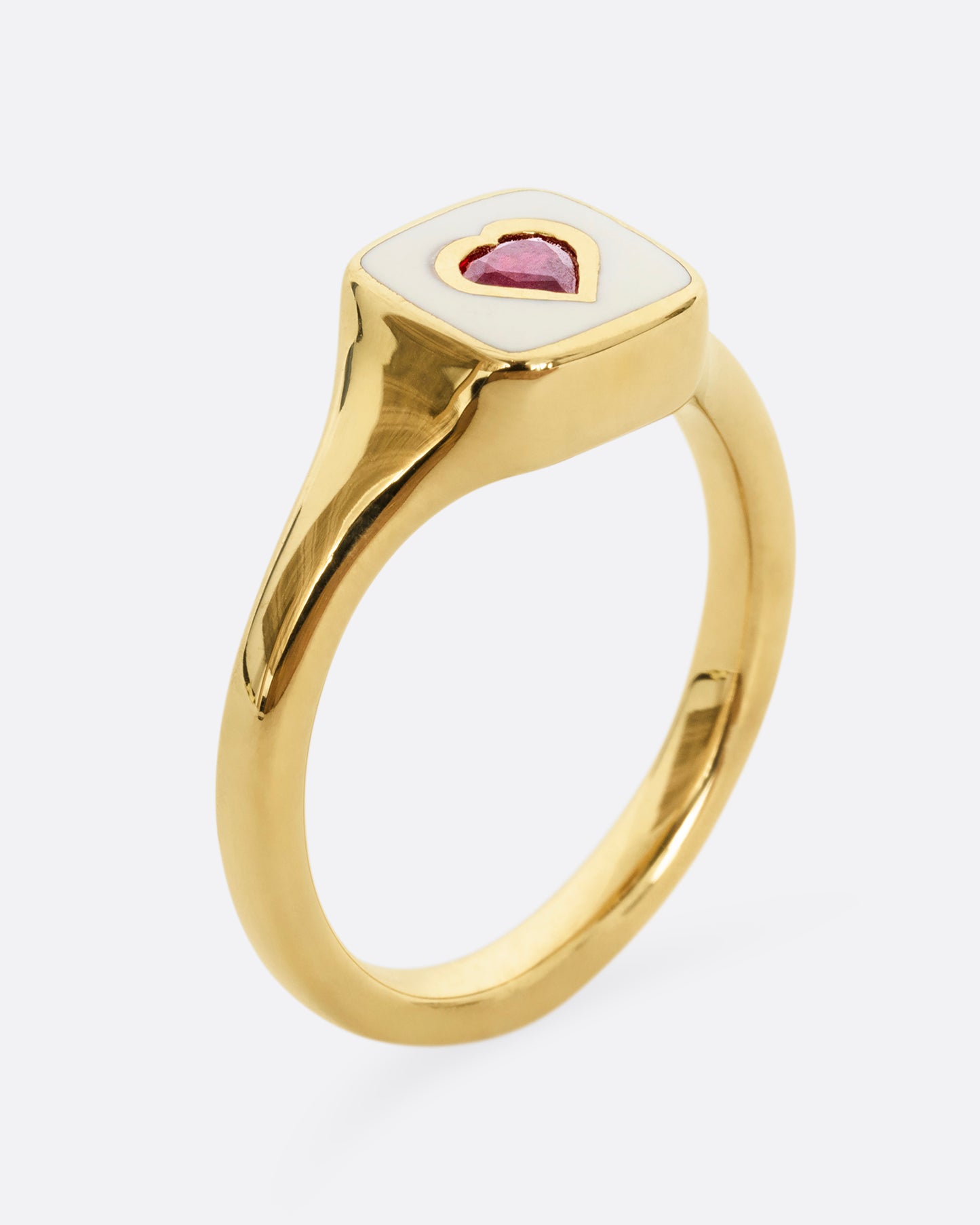 A yellow gold signet ring with cream enamel and a heart shaped ruby. Shown from the side, standing up.