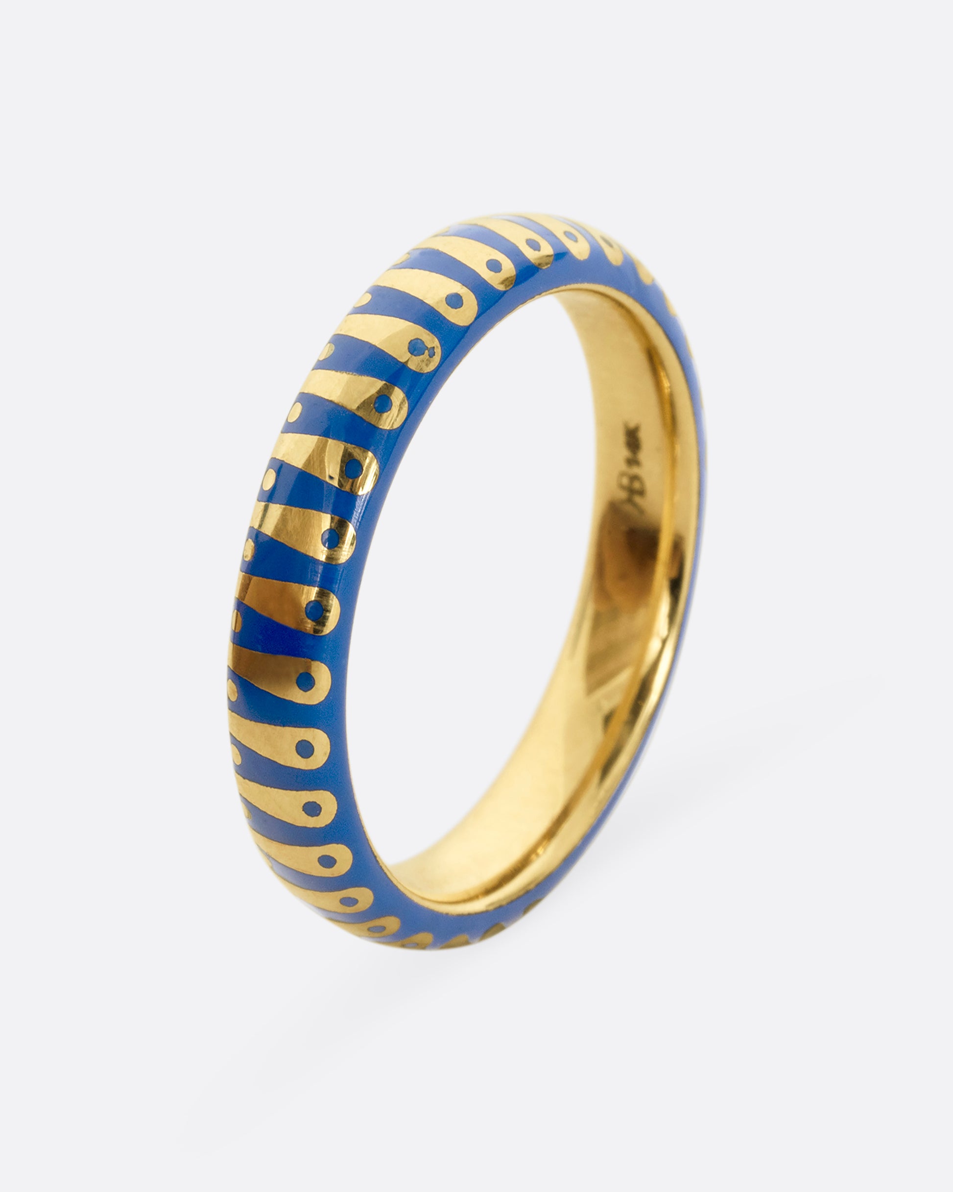 A yellow gold band ring with cobalt blue enamel stripes and dots. Shown from the side.