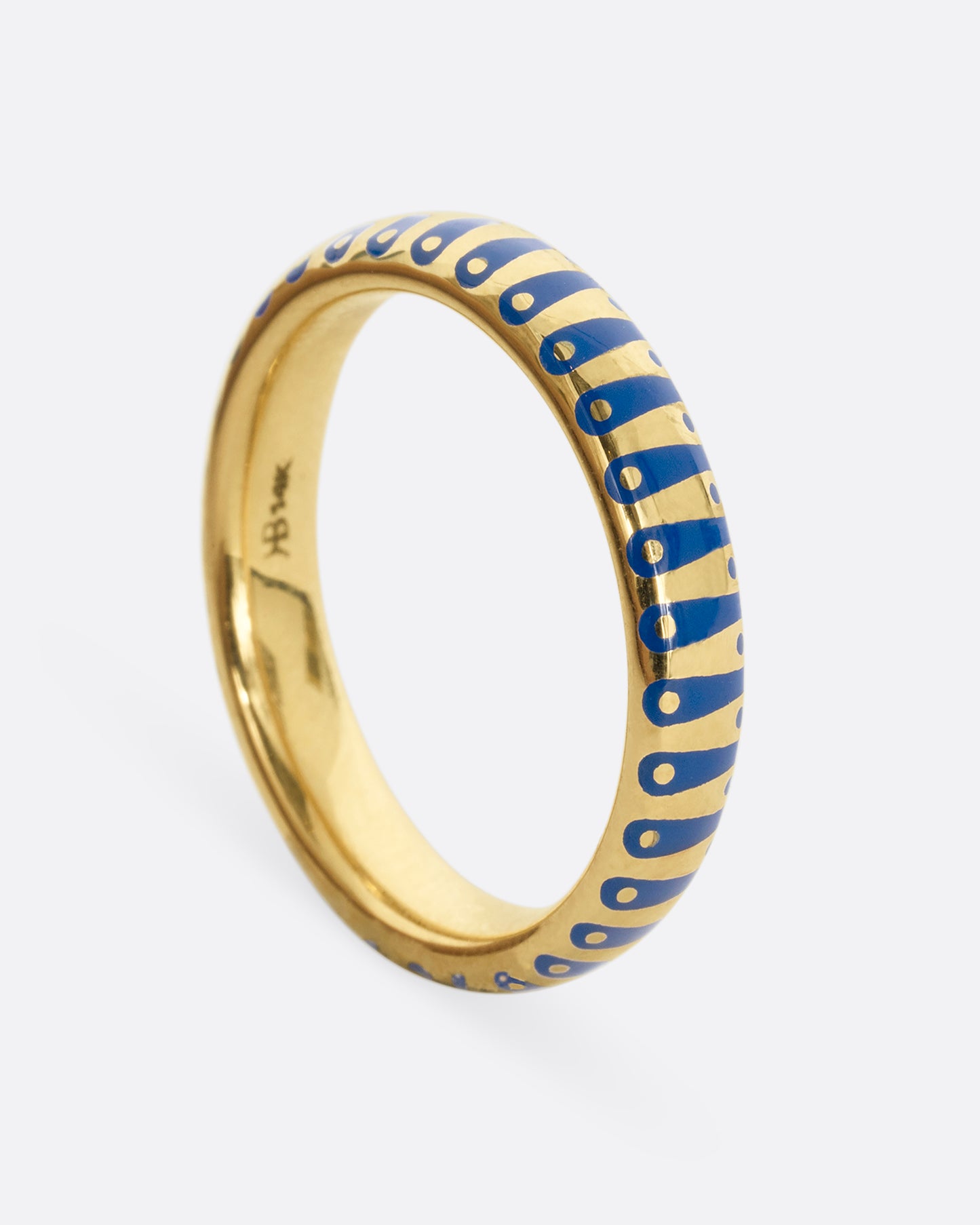 A yellow gold band ring with cobalt blue enamel stripes and dots. Shown from the side.