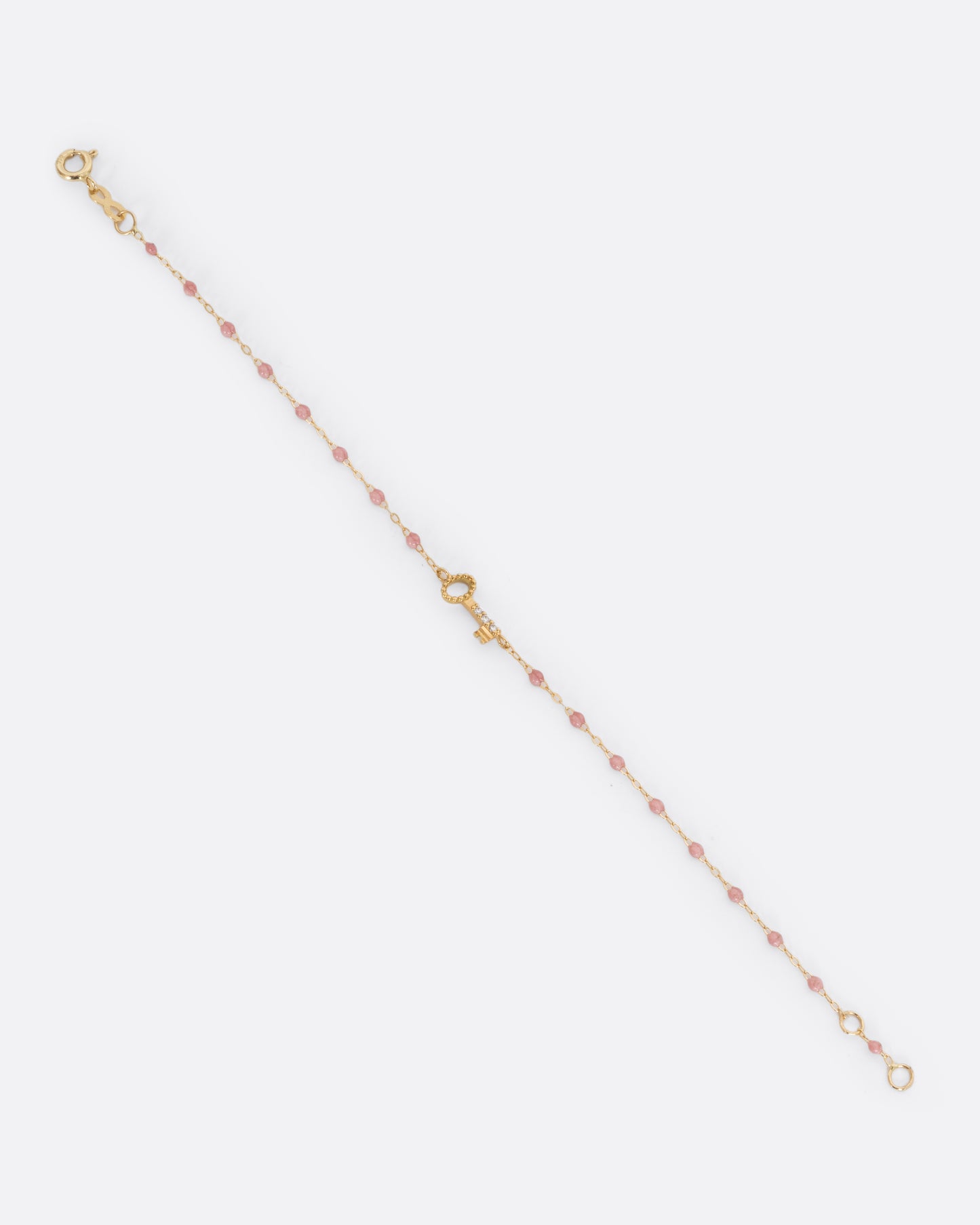 A yellow gold cable chain bracelet with droplets of pink resin and a yellow gold key charm. Three white diamonds are set on the key charm. Shown unclasped from the front.