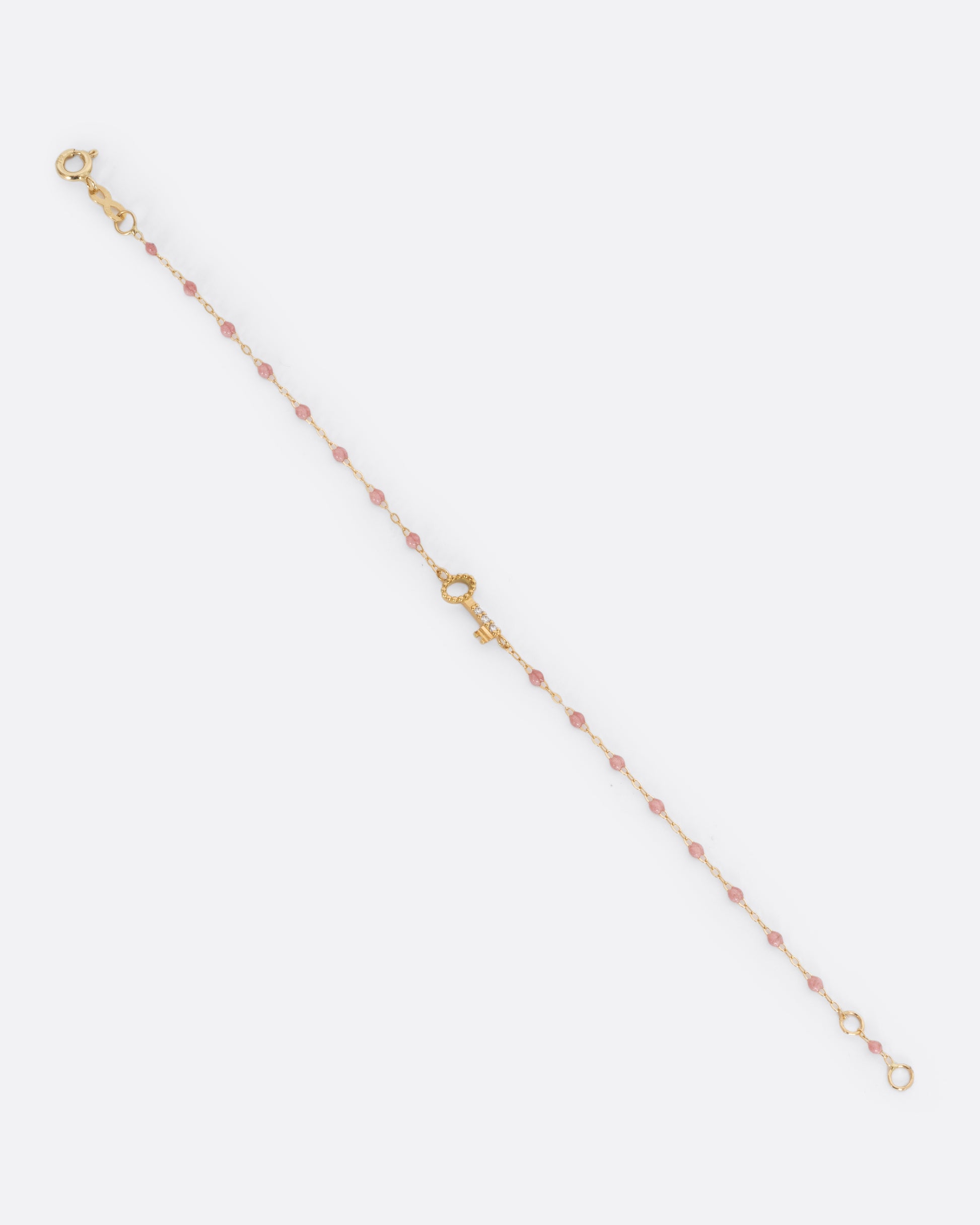 A yellow gold cable chain bracelet with droplets of pink resin and a yellow gold key charm. Three white diamonds are set on the key charm. Shown unclasped from the front.