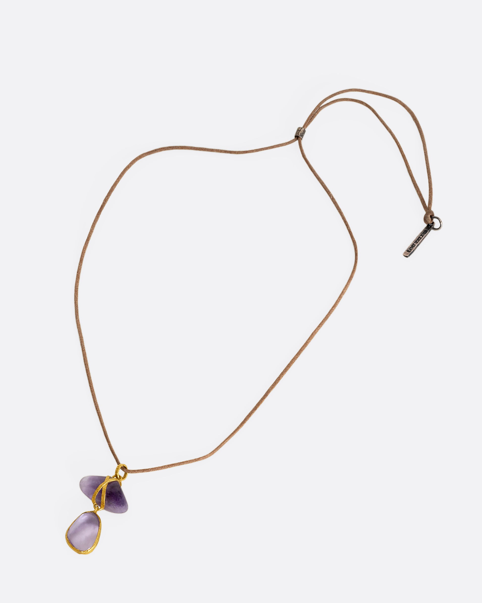 An amethyst pendant wrapped in high karat yellow gold hanging from a cord necklace. Shown laying flat.