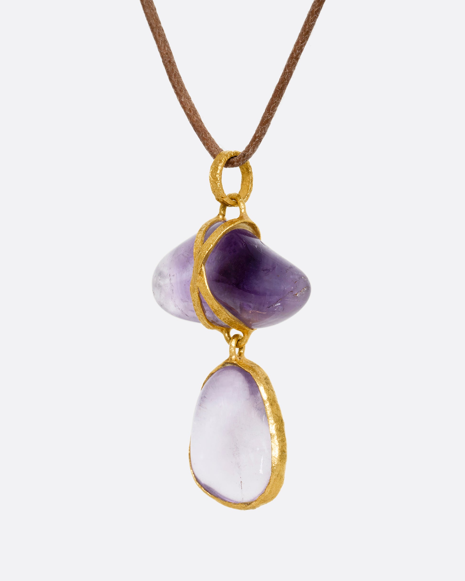 An amethyst pendant wrapped in high karat yellow gold hanging from a cord necklace. Shown from the side.