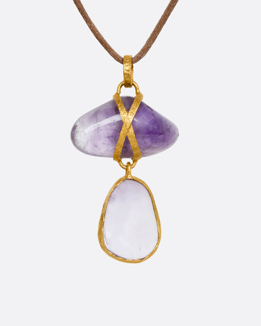 An amethyst pendant wrapped in high karat yellow gold hanging from a cord necklace. Shown from the front.