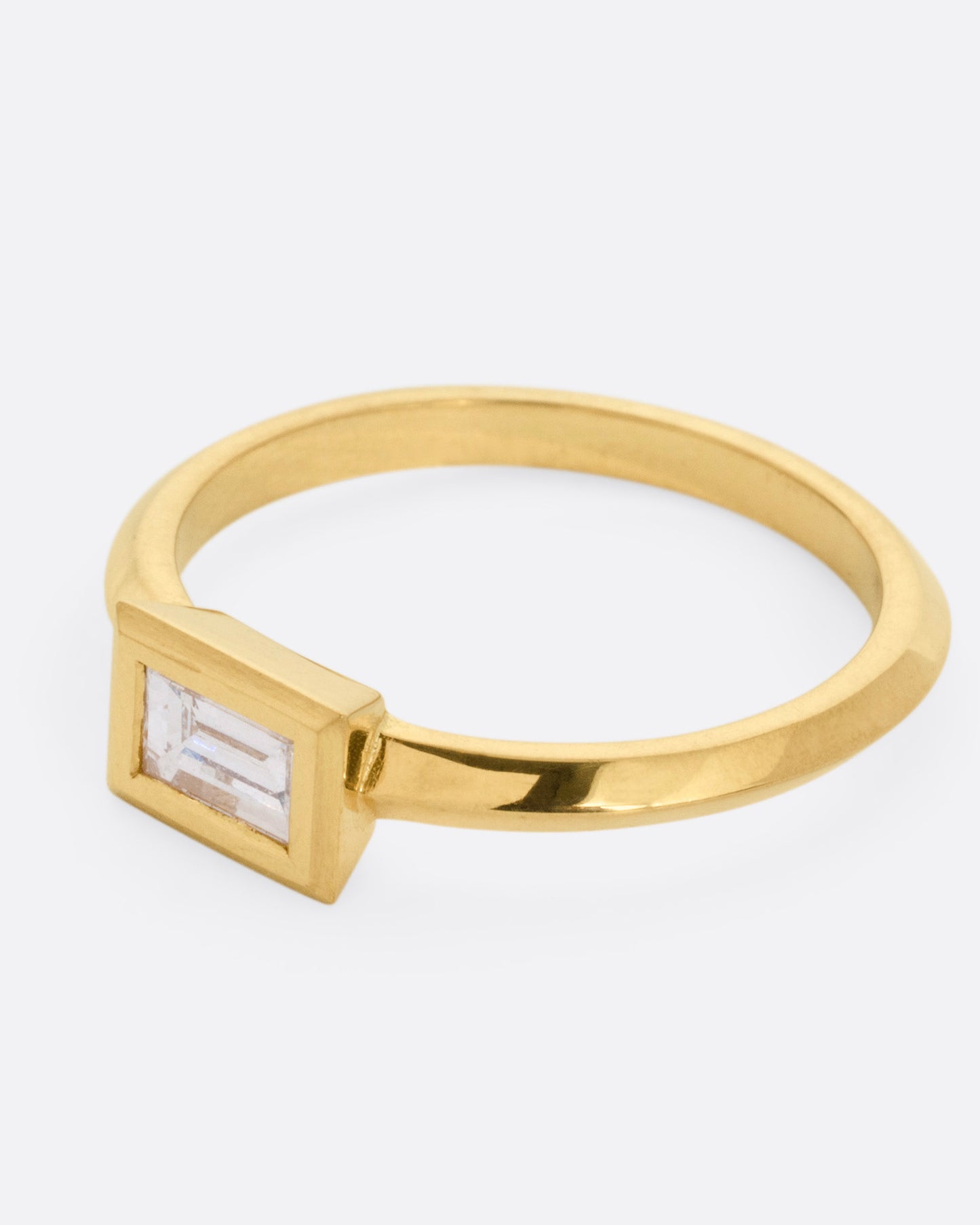 A yellow gold ring with a baguette diamond, shown from the side.