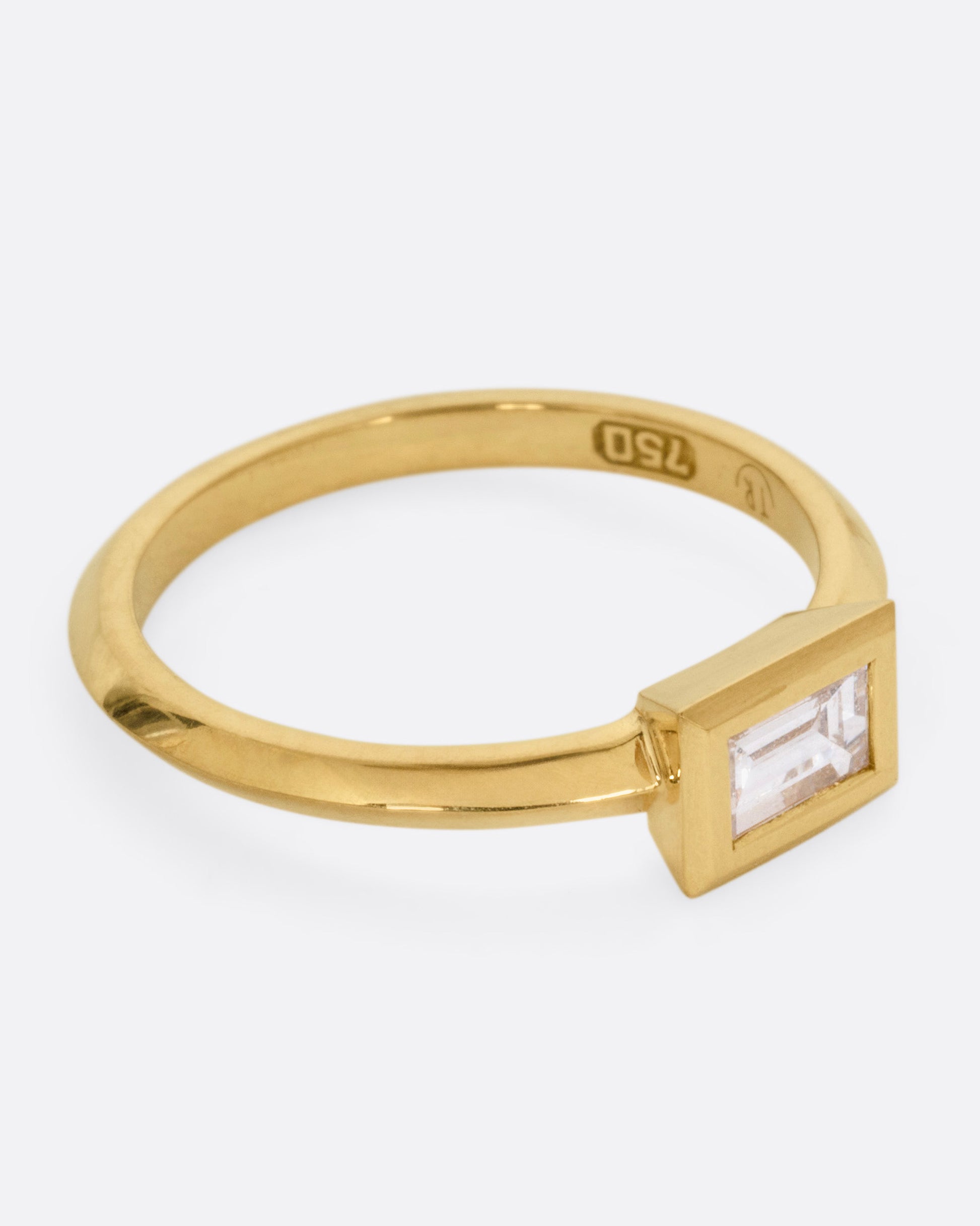 A yellow gold ring with a baguette diamond, shown from the side.