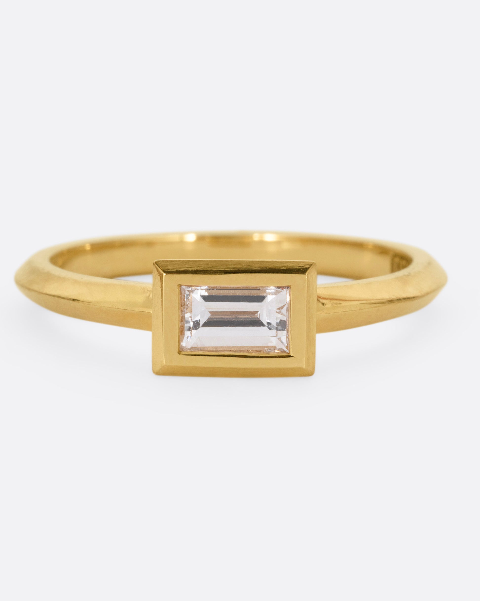 A yellow gold ring with a baguette diamond, shown from the front.