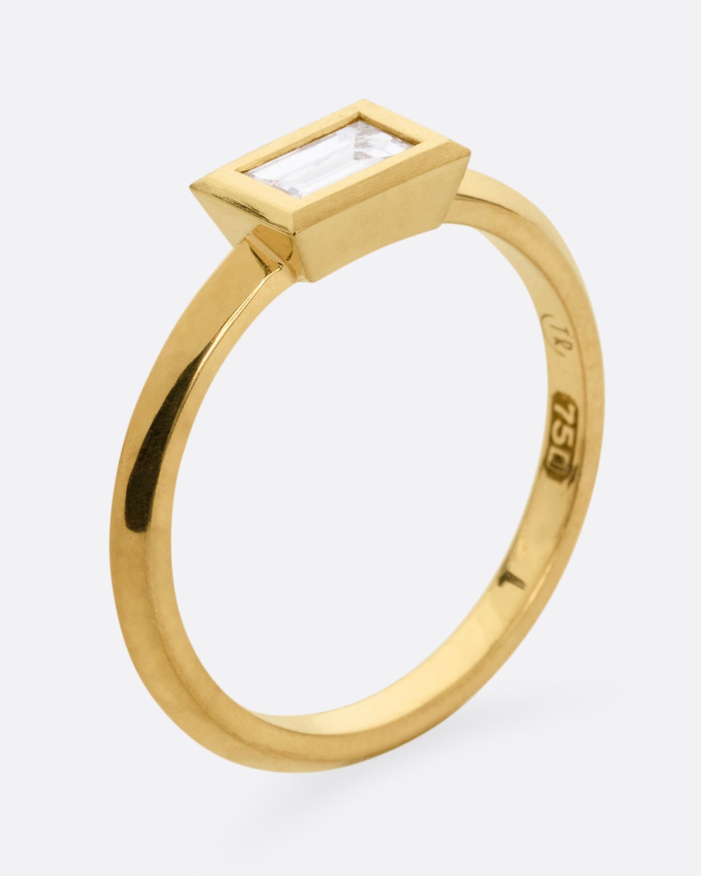 A yellow gold ring with a baguette diamond, shown from the side standing up.