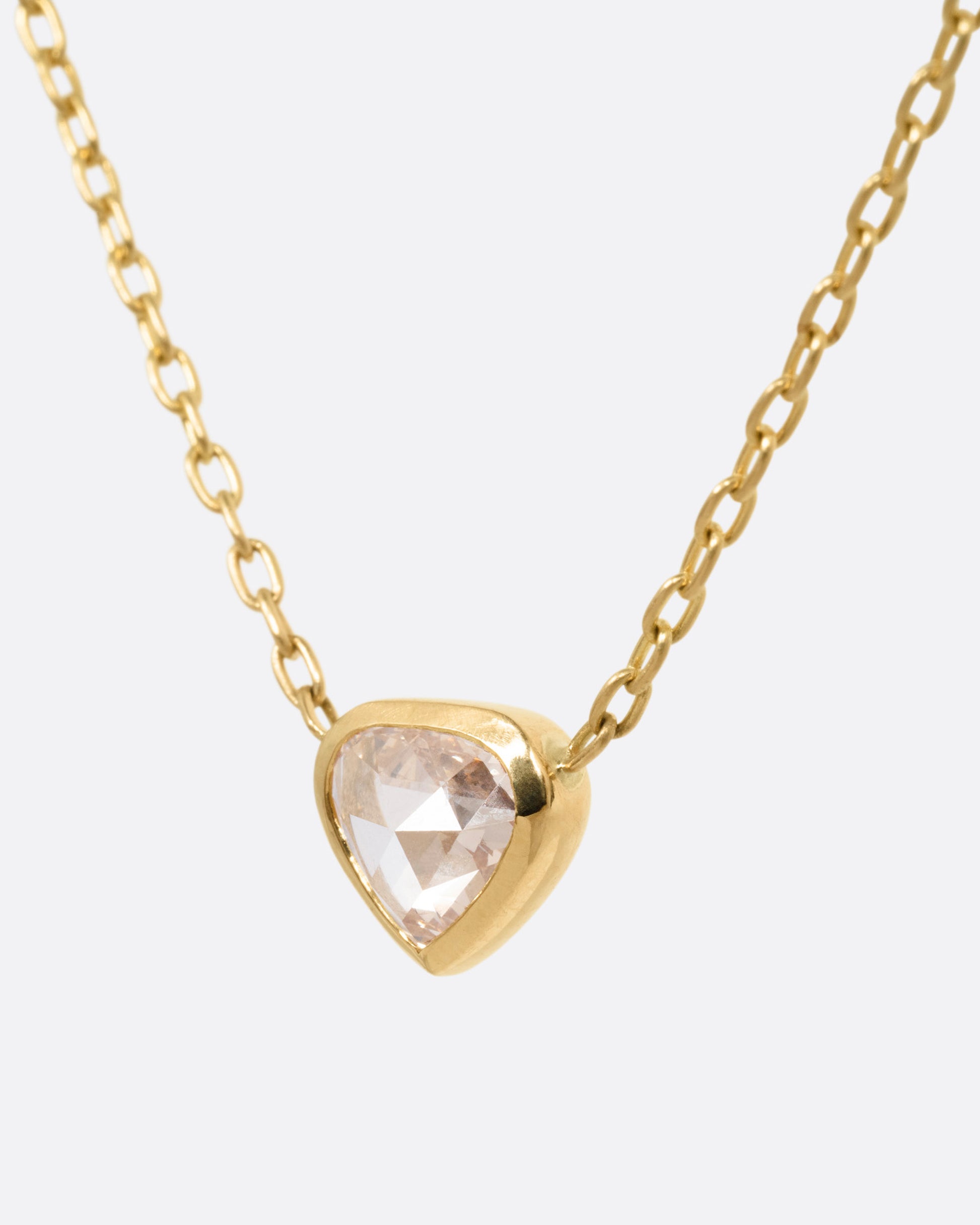 A yellow gold necklace with a natural organic heart shaped diamond, shown from the side.