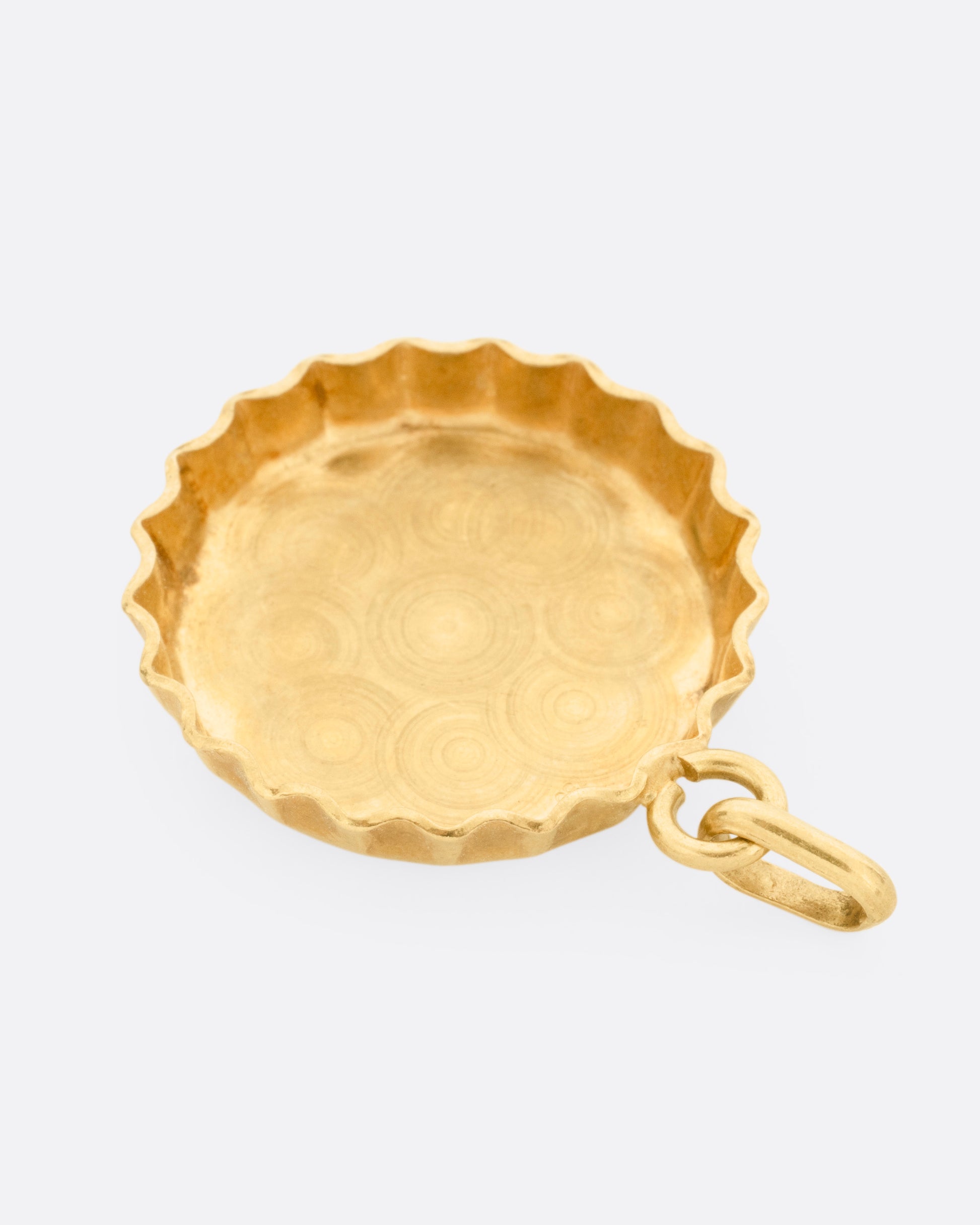 A yellow gold bottle cap charm, shown from the back.