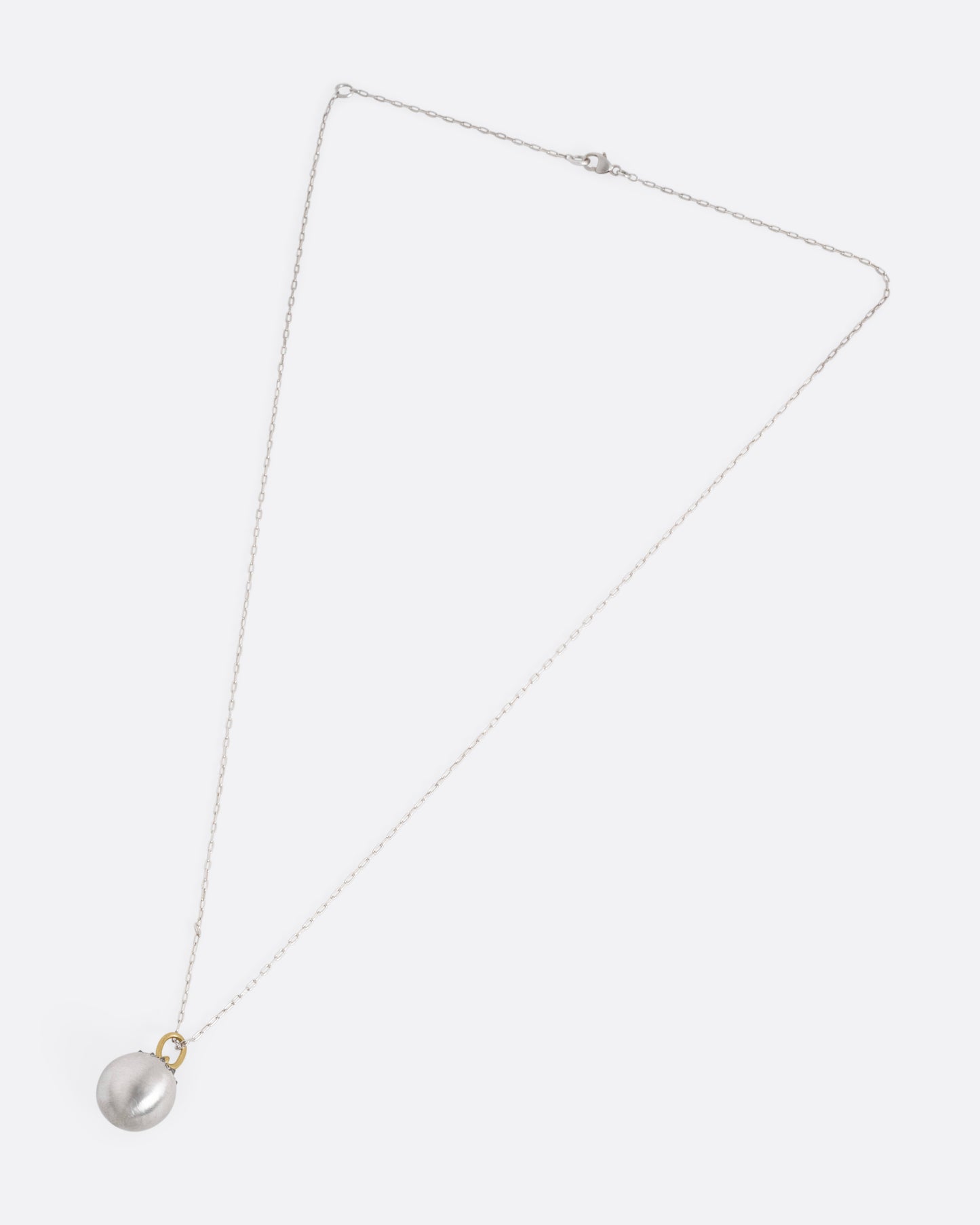 A silver cable chain necklace with a sizable sterling orb pendant peppered with grey reverse set diamonds and a yellow gold bail, shown from the front.