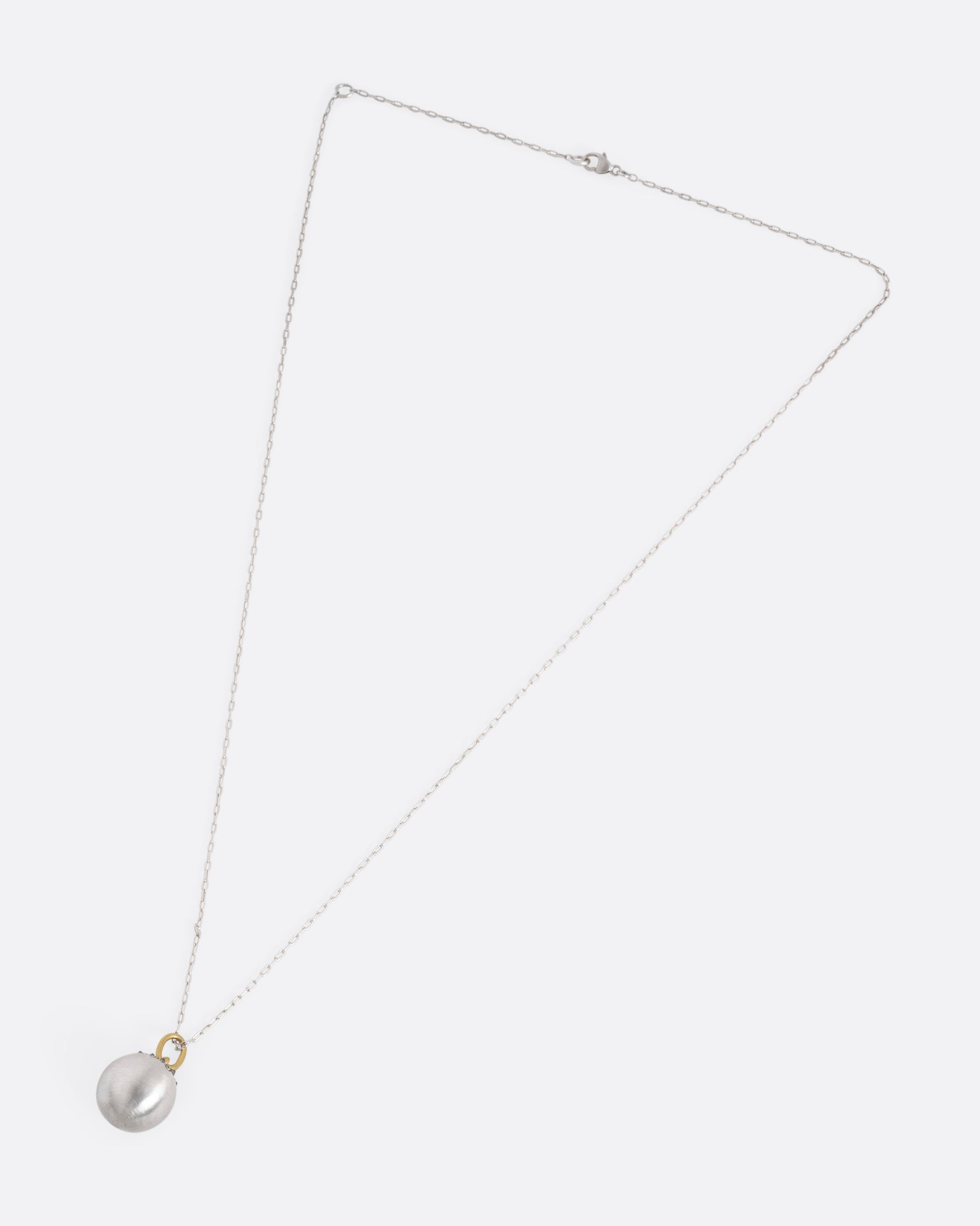 A silver cable chain necklace with a sizable sterling orb pendant peppered with grey reverse set diamonds and a yellow gold bail, shown from the front.