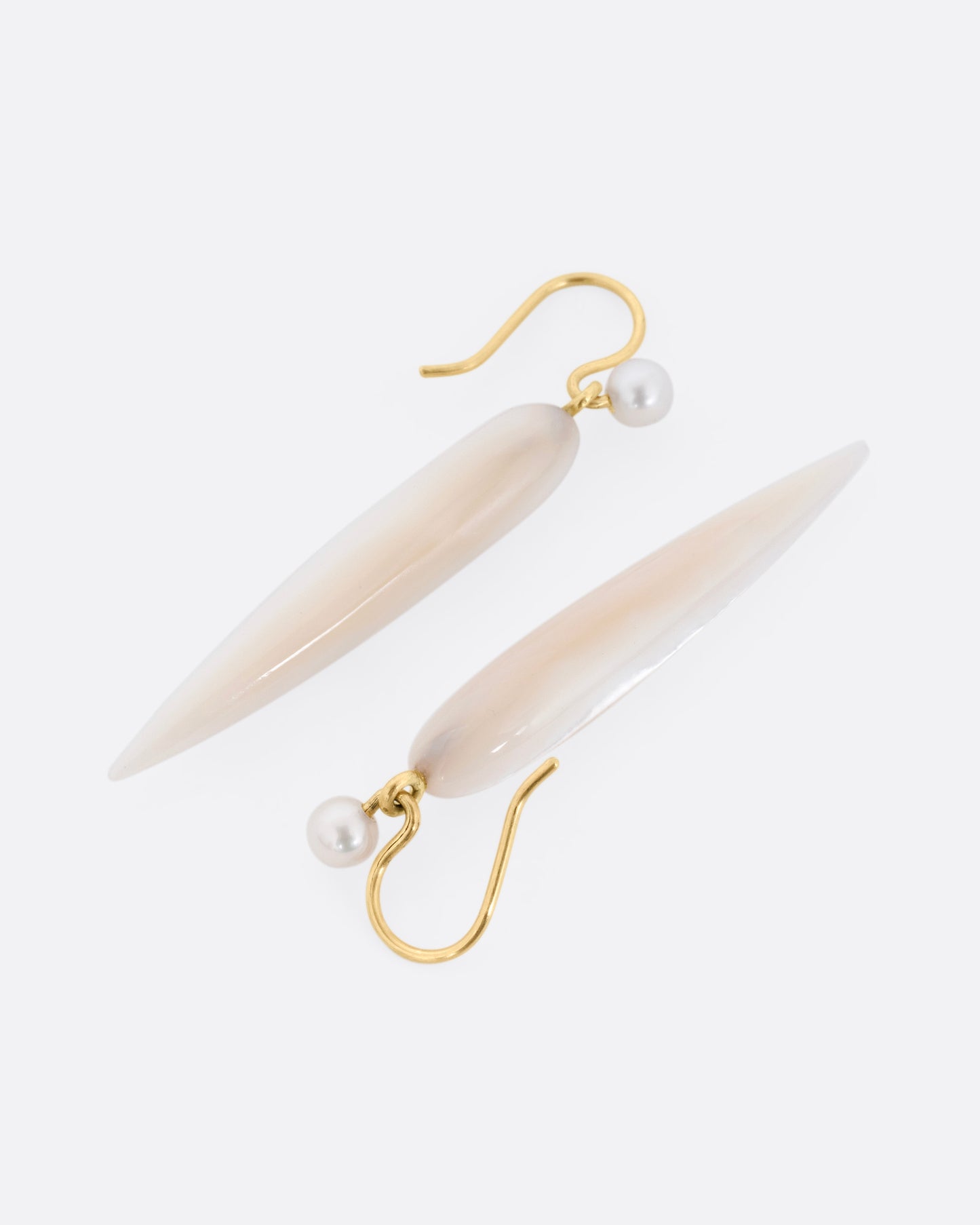 A pair of pointed mother of pearl drop earring with yellow gold ear hooks, shown lying flat.