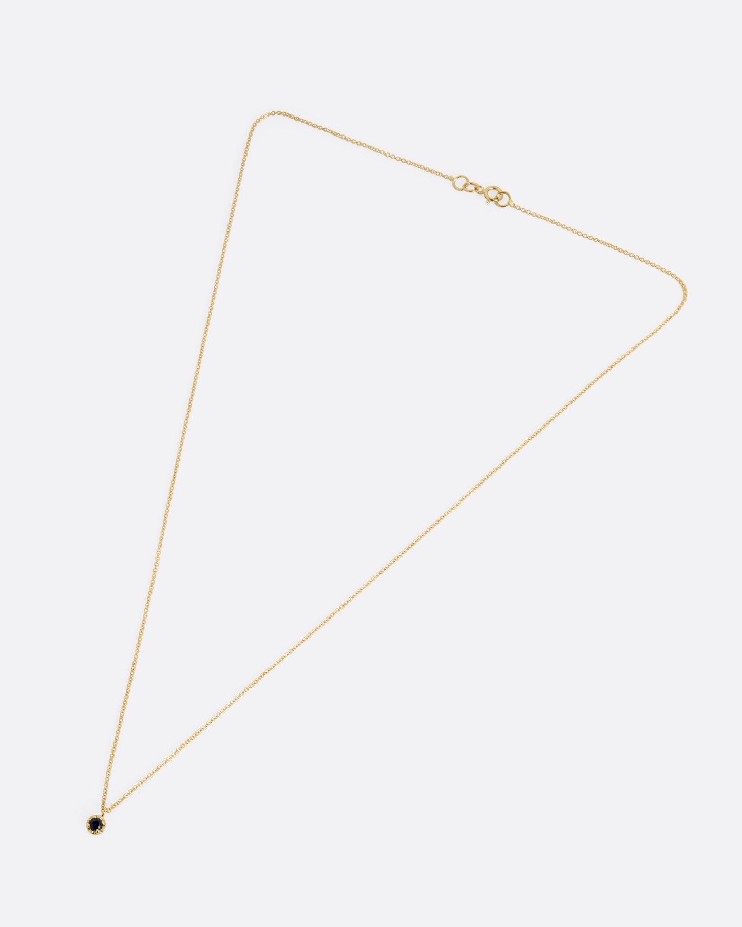 A yellow gold cable chain necklace with a  prong set sapphire, shown from the front.