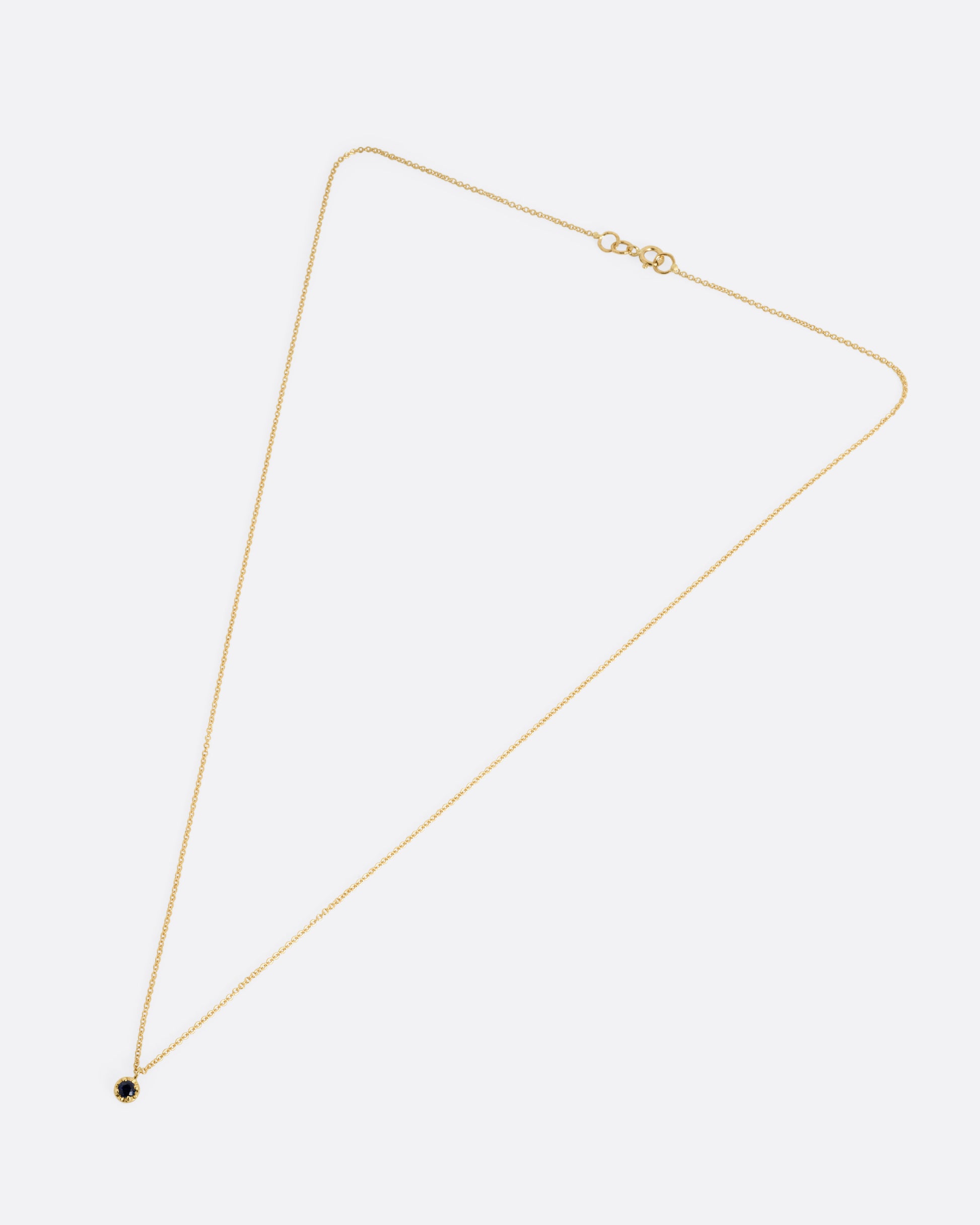 A yellow gold cable chain necklace with a  prong set sapphire, shown from the front.