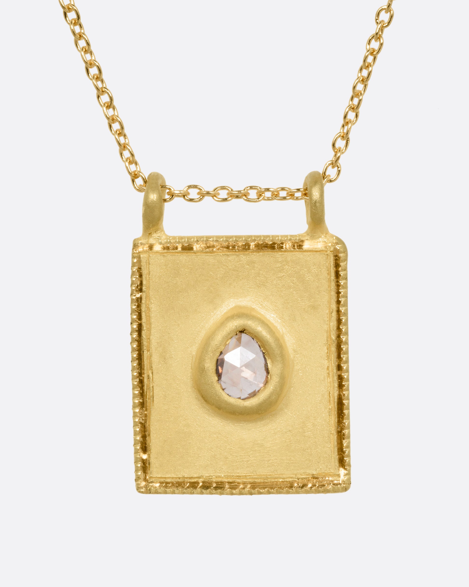 A yellow gold pendant necklace with a teardrop shaped salt and pepper diamond in a rectangular gold frame, with a double bail. Shown from the front.