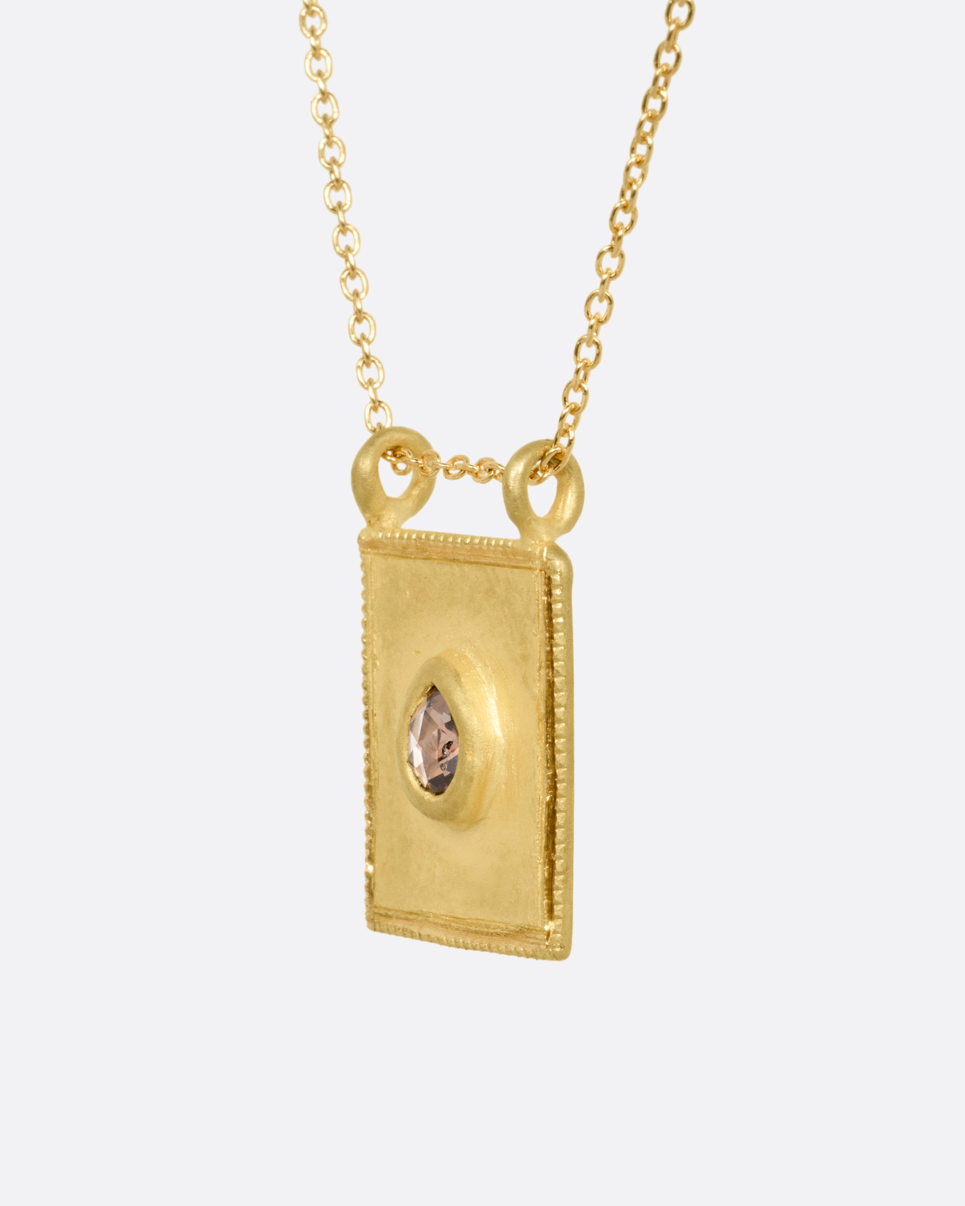 A yellow gold pendant necklace with a teardrop shaped salt and pepper diamond in a rectangular gold frame, with a double bail. Shown from the side.