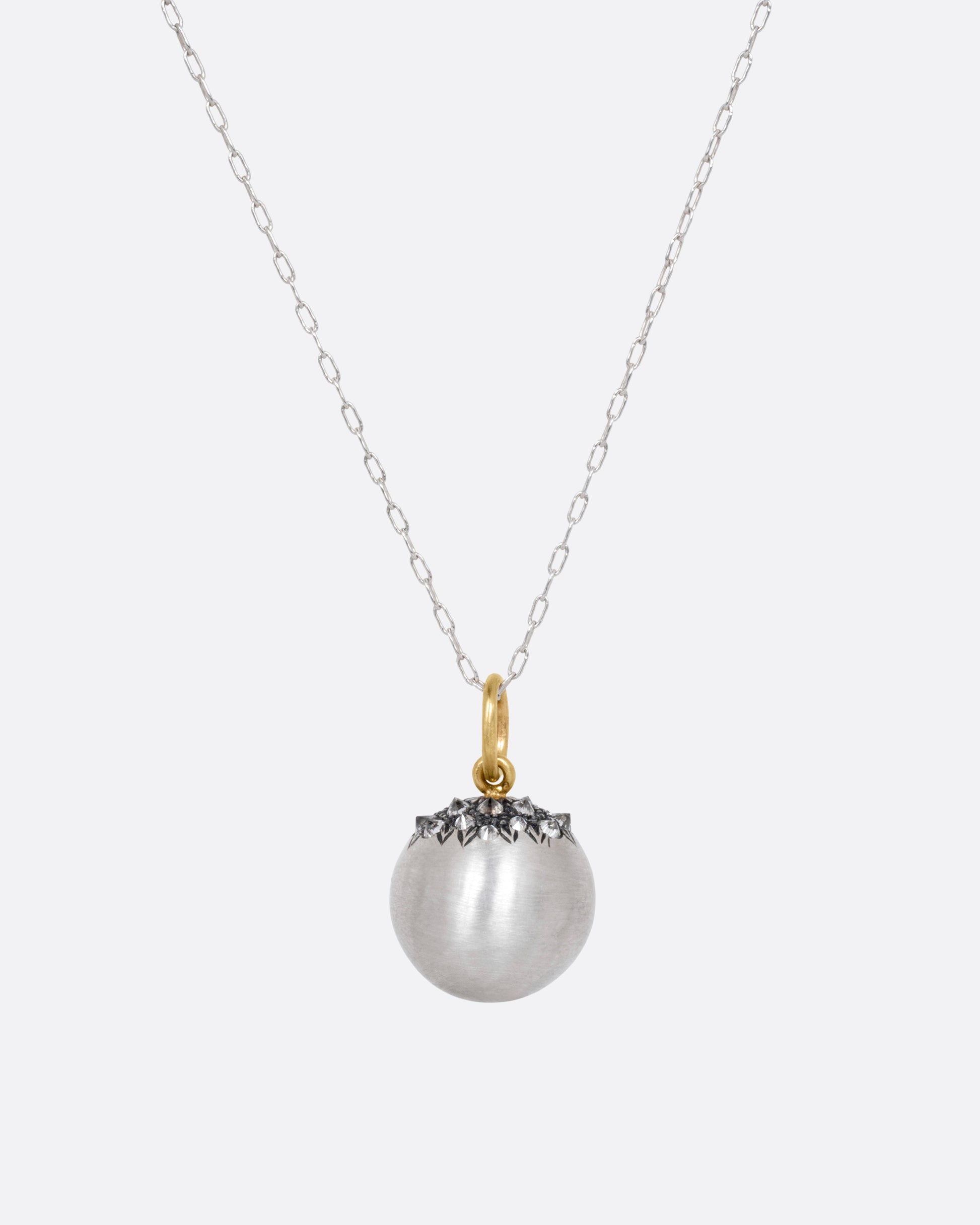 A silver cable chain necklace with a sizable sterling orb pendant peppered with grey reverse set diamonds and a yellow gold bail, shown from the front.