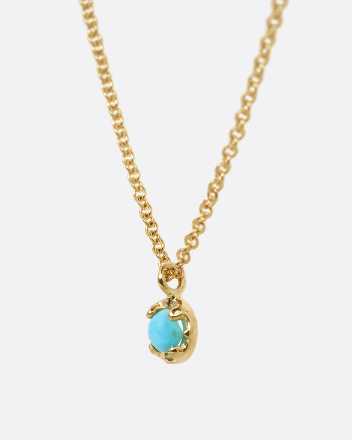 A yellow gold cable chain necklace with a  prong set turquoise, shown from the side.