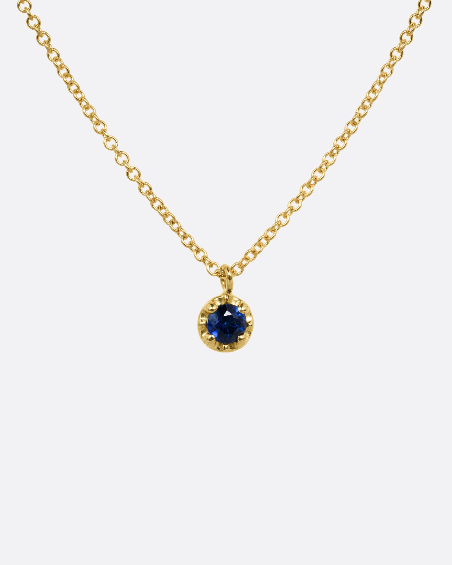 A yellow gold cable chain necklace with a  prong set sapphire, shown from the front.