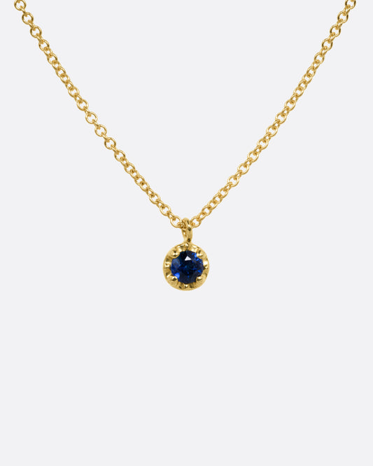 A yellow gold cable chain necklace with a  prong set sapphire, shown from the front.