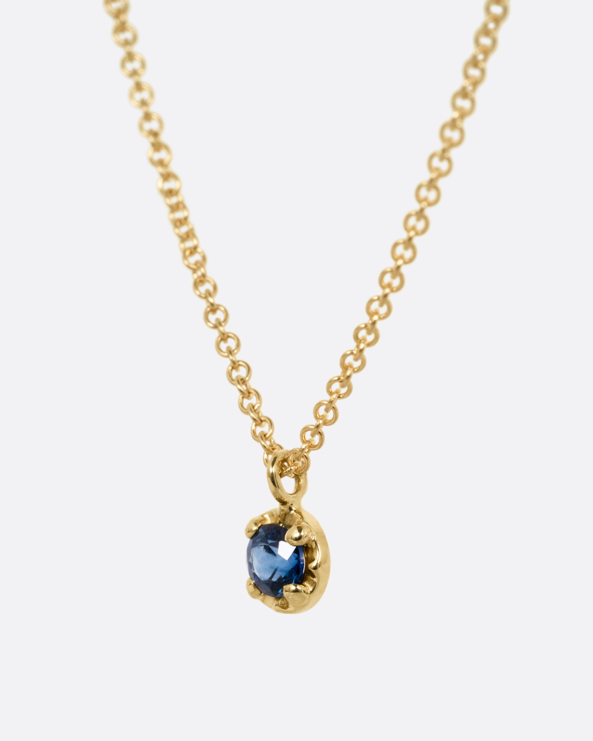 A yellow gold cable chain necklace with a  prong set sapphire, shown from the side.